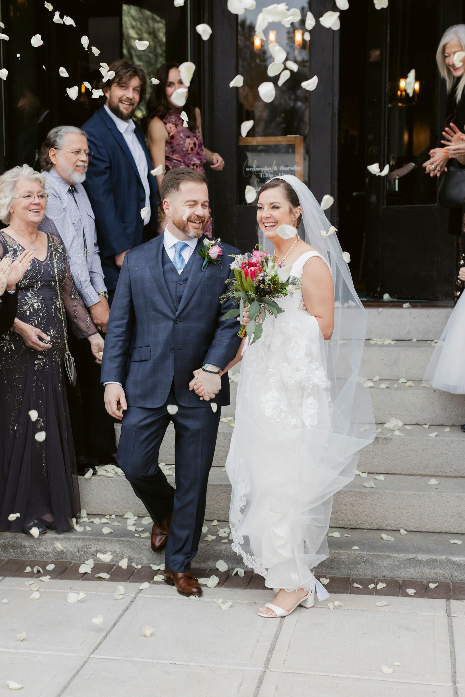 Wedding guests celebrate by throwing rose petals outside a venue with festive decorations.