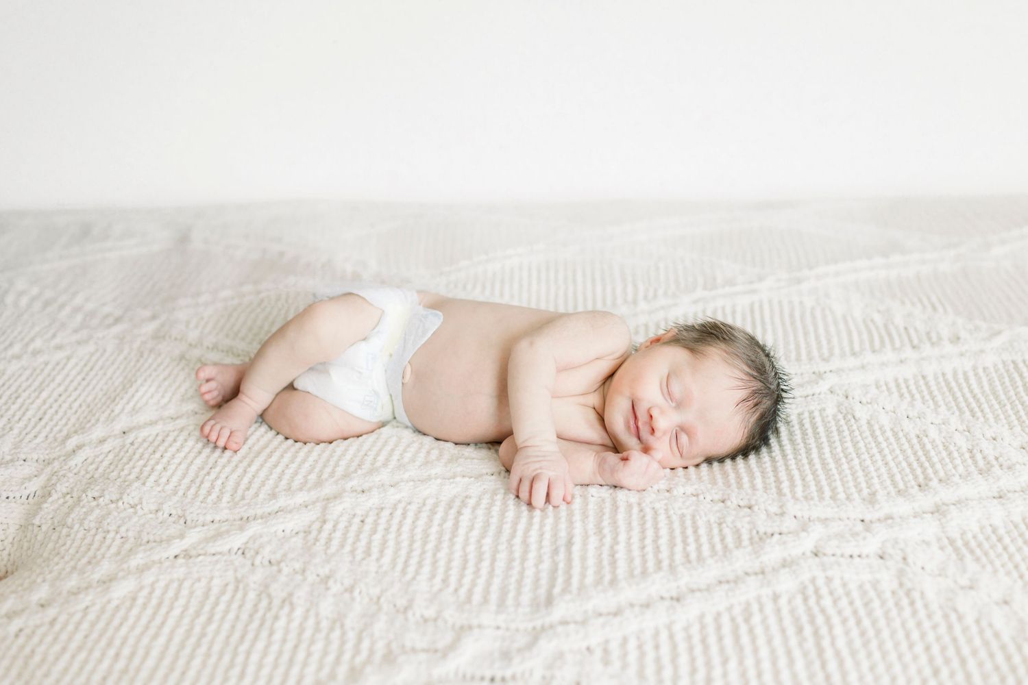 Peaceful newborn sleeping on white textured bedding.