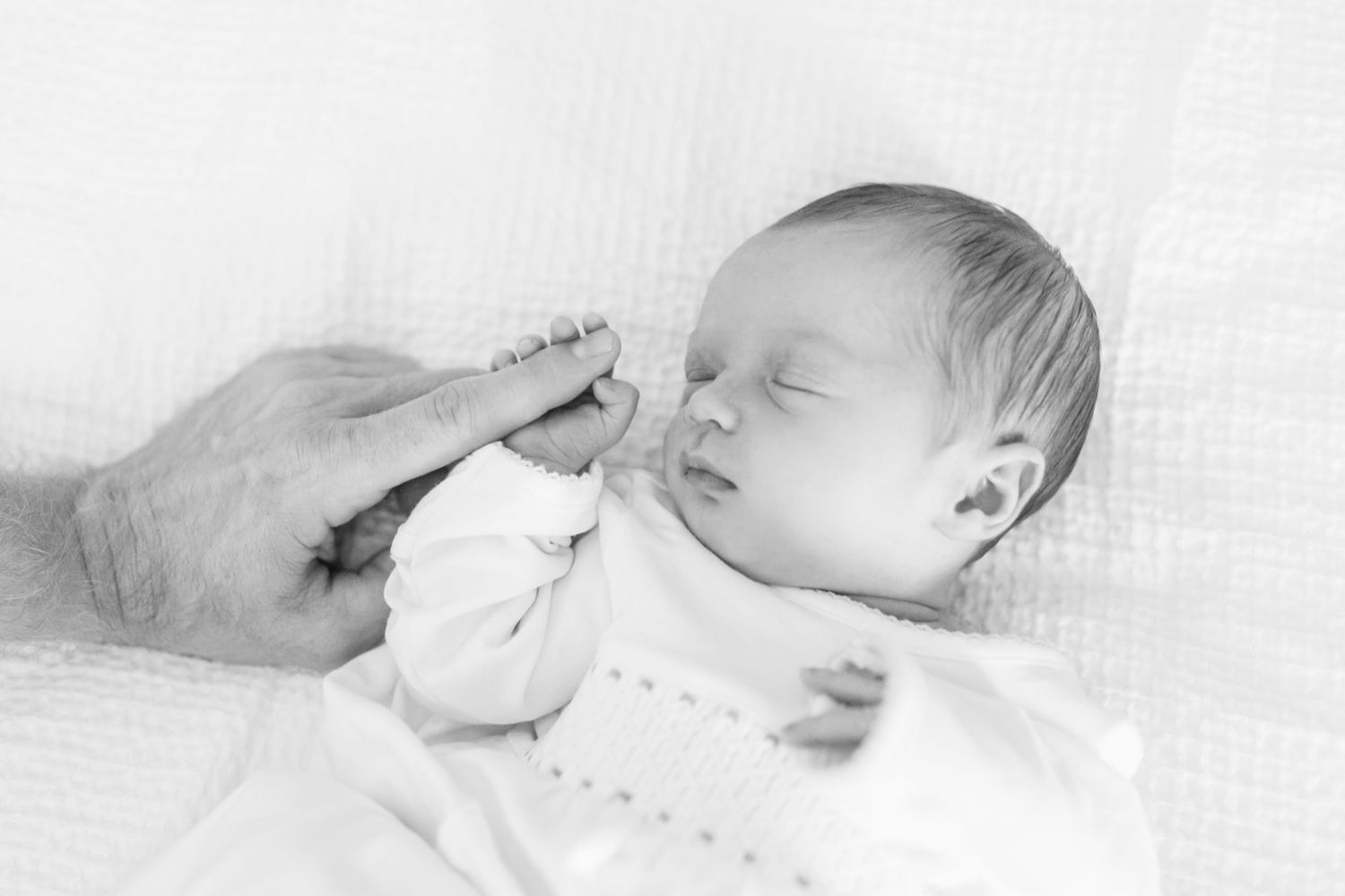 Black and white image of a tiny sleeping newborn being gently touched on the forehead.