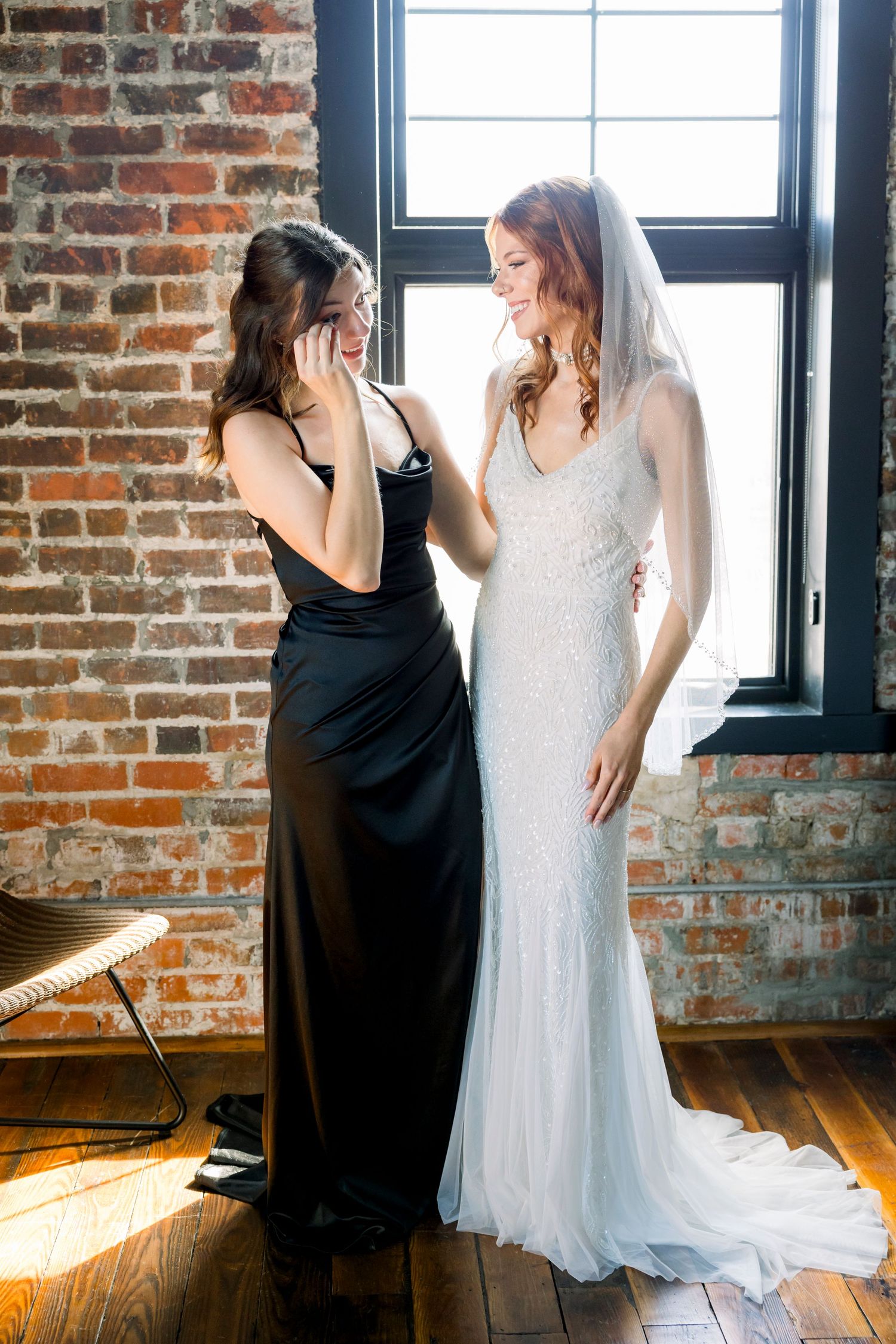 Two figures in contrasting black and white dresses pose in front of exposed brick and windows.