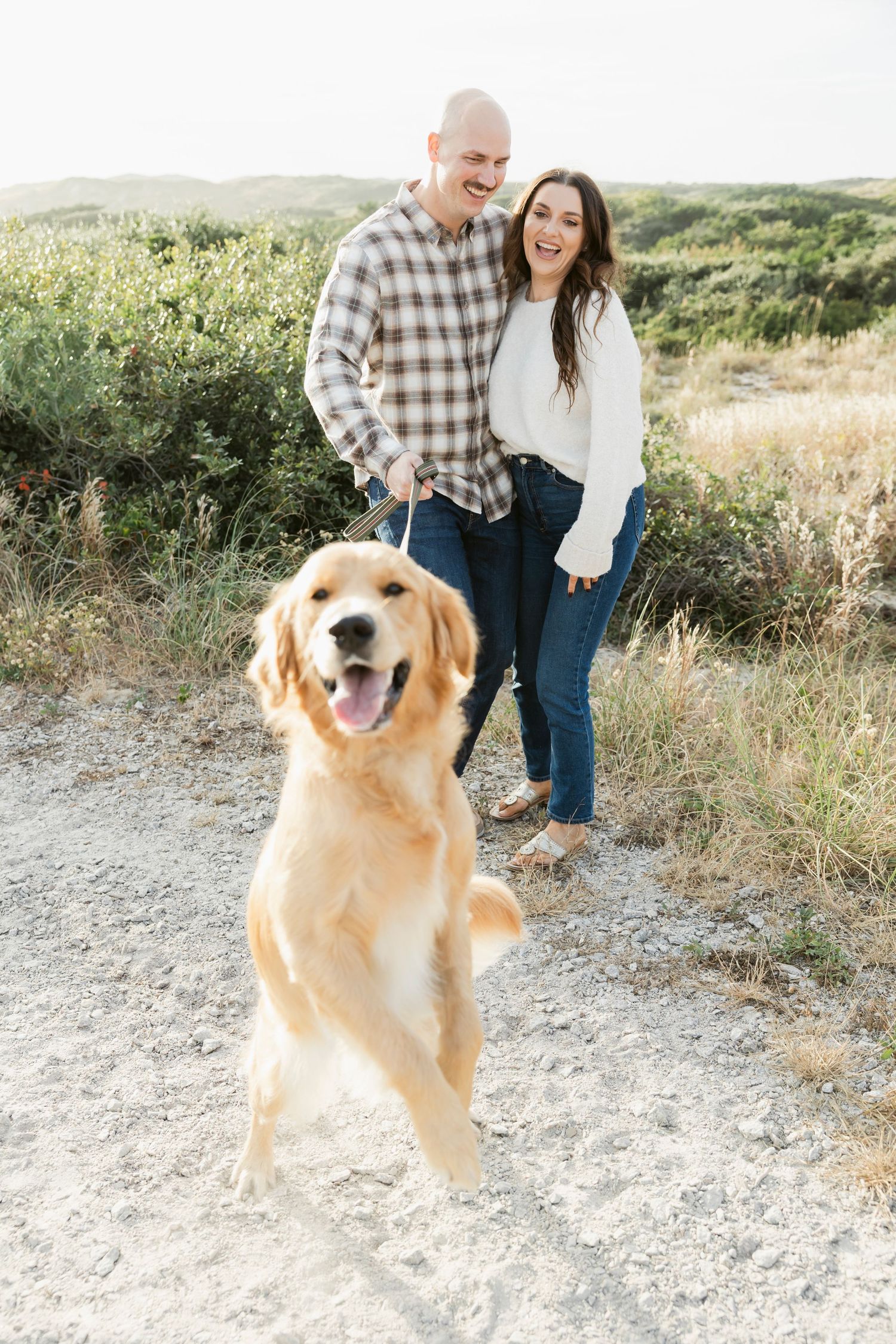 A happy golden retriever jumps playfully during an outdoor couples photoshoot.