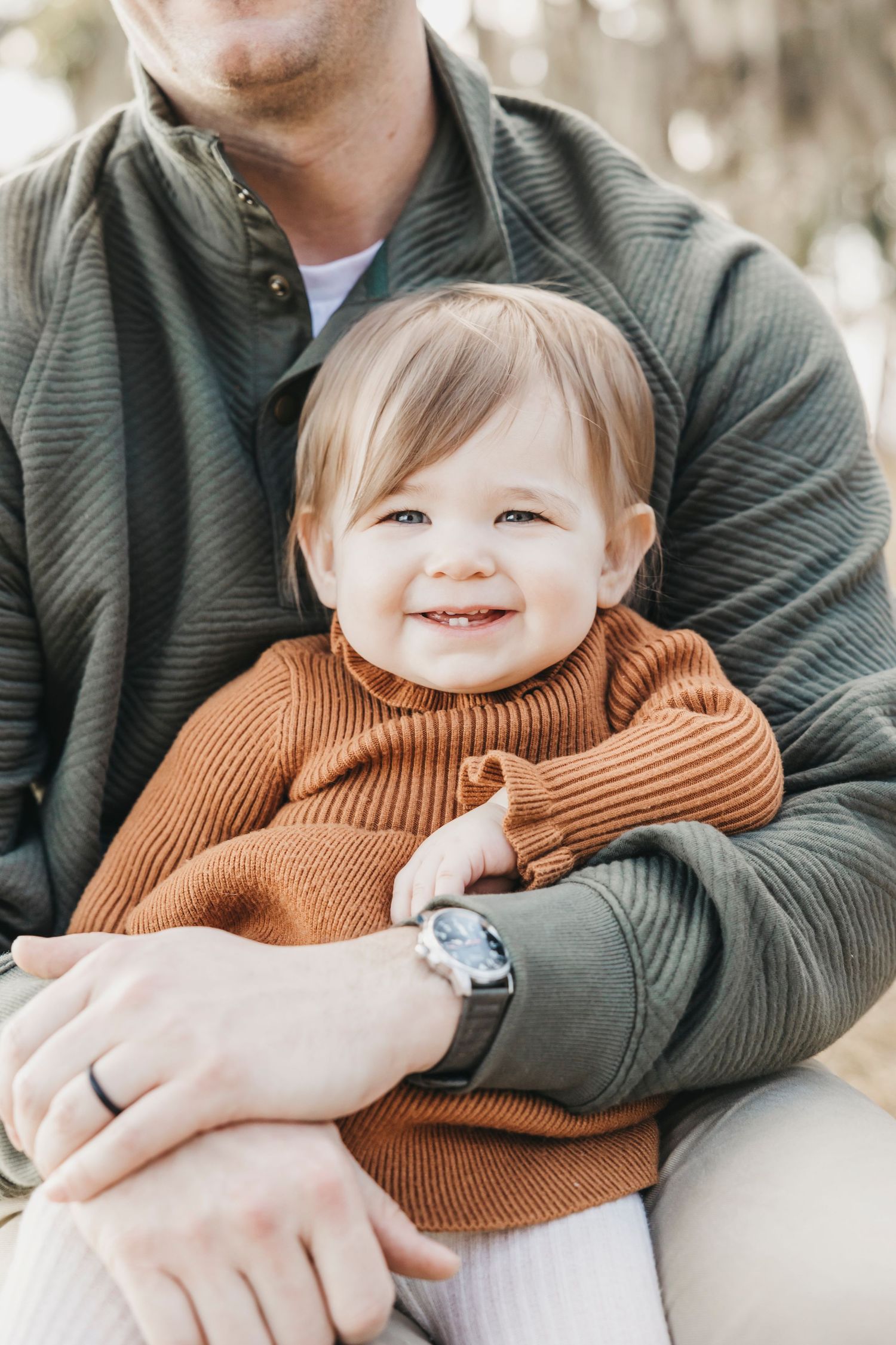 Parent in gray sweater hugging small child wearing brown knit sweater in heartwarming candid moment.
