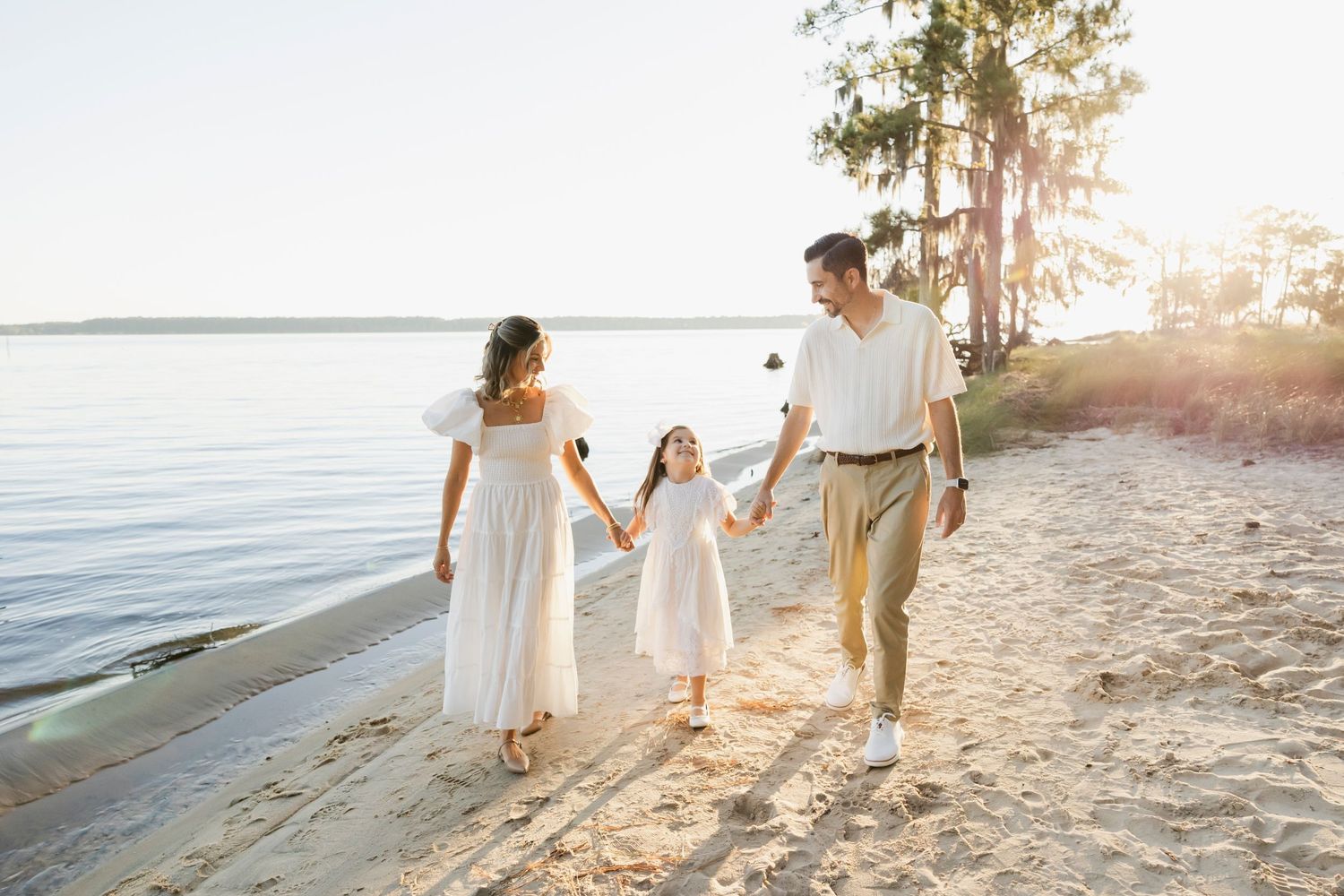 Family walking together on sandy beach at sunset with warm golden light.