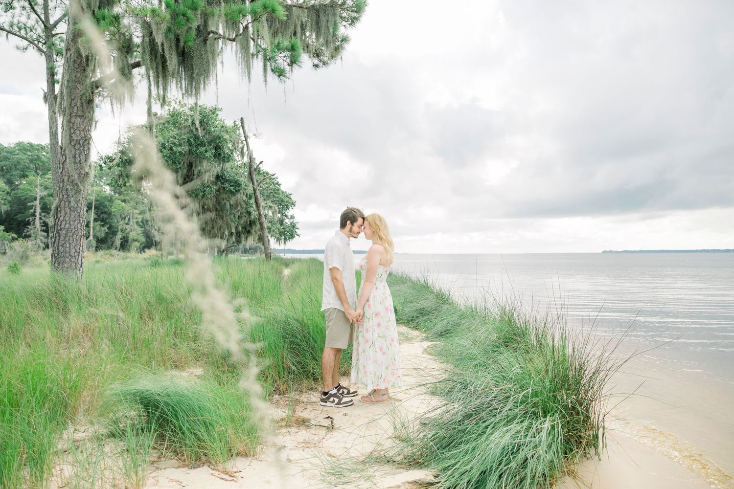 Couple walking along a scenic beach boardwalk surrounded by tall grass and dunes at sunset.