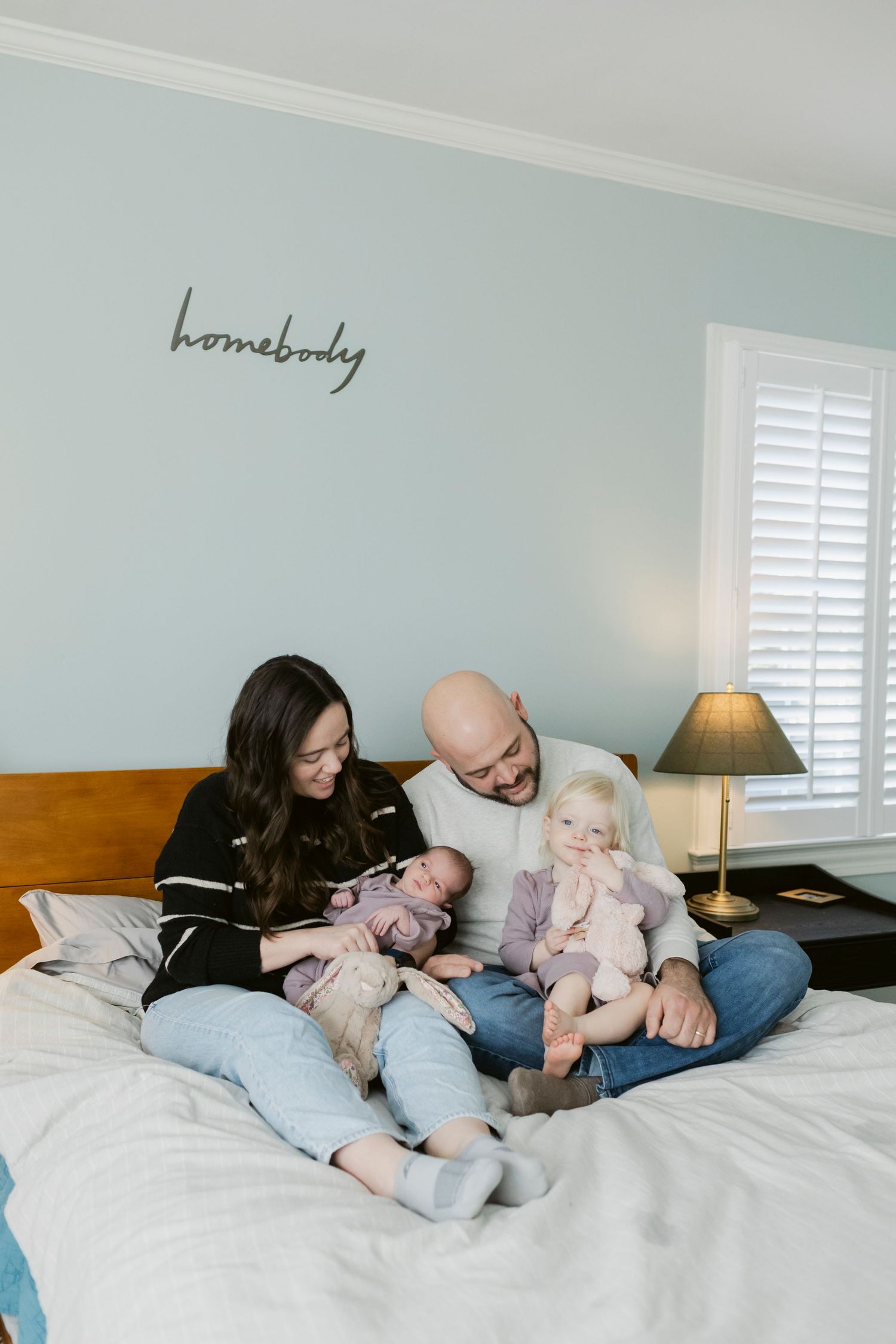 Family relaxing together on bed with light blue walls and wooden headboard.