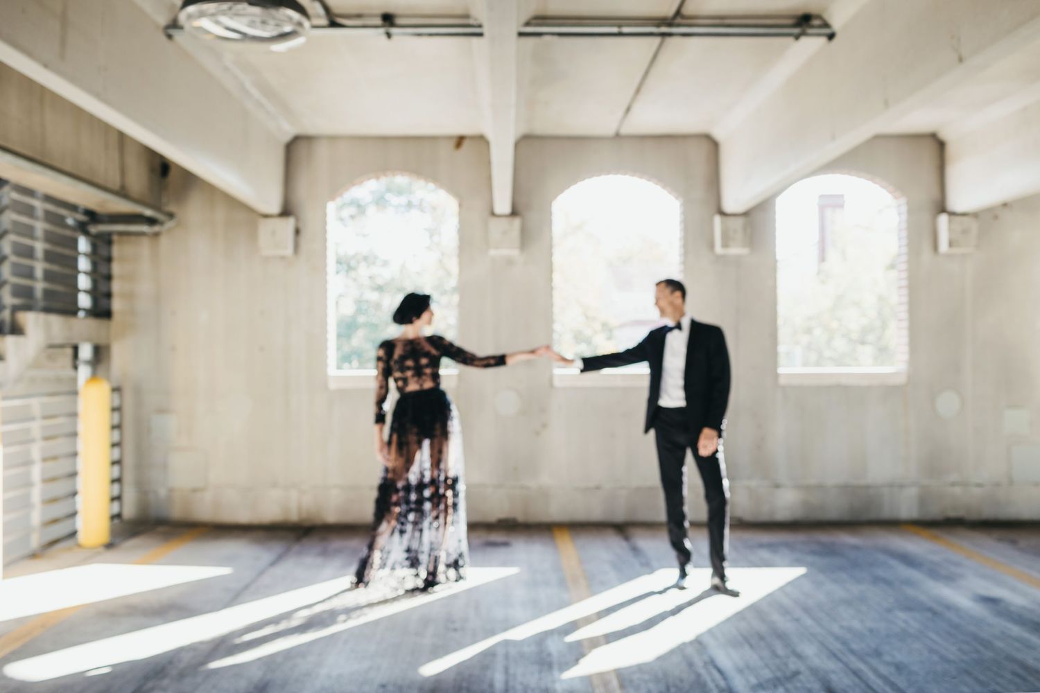 Couple playfully dancing in an empty industrial warehouse space with natural light streaming through windows.