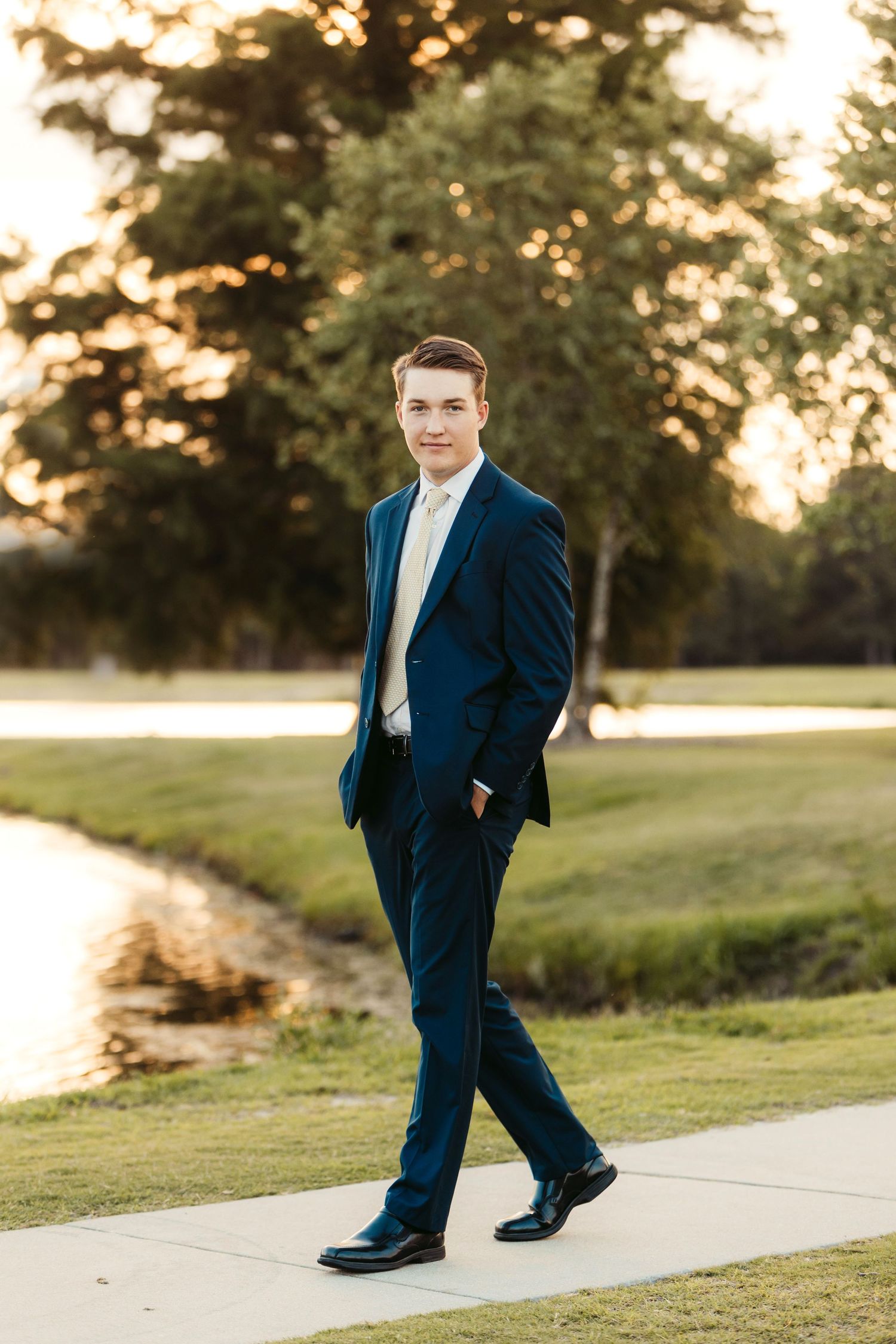 Full length photo of person in navy suit walking on path during golden hour.