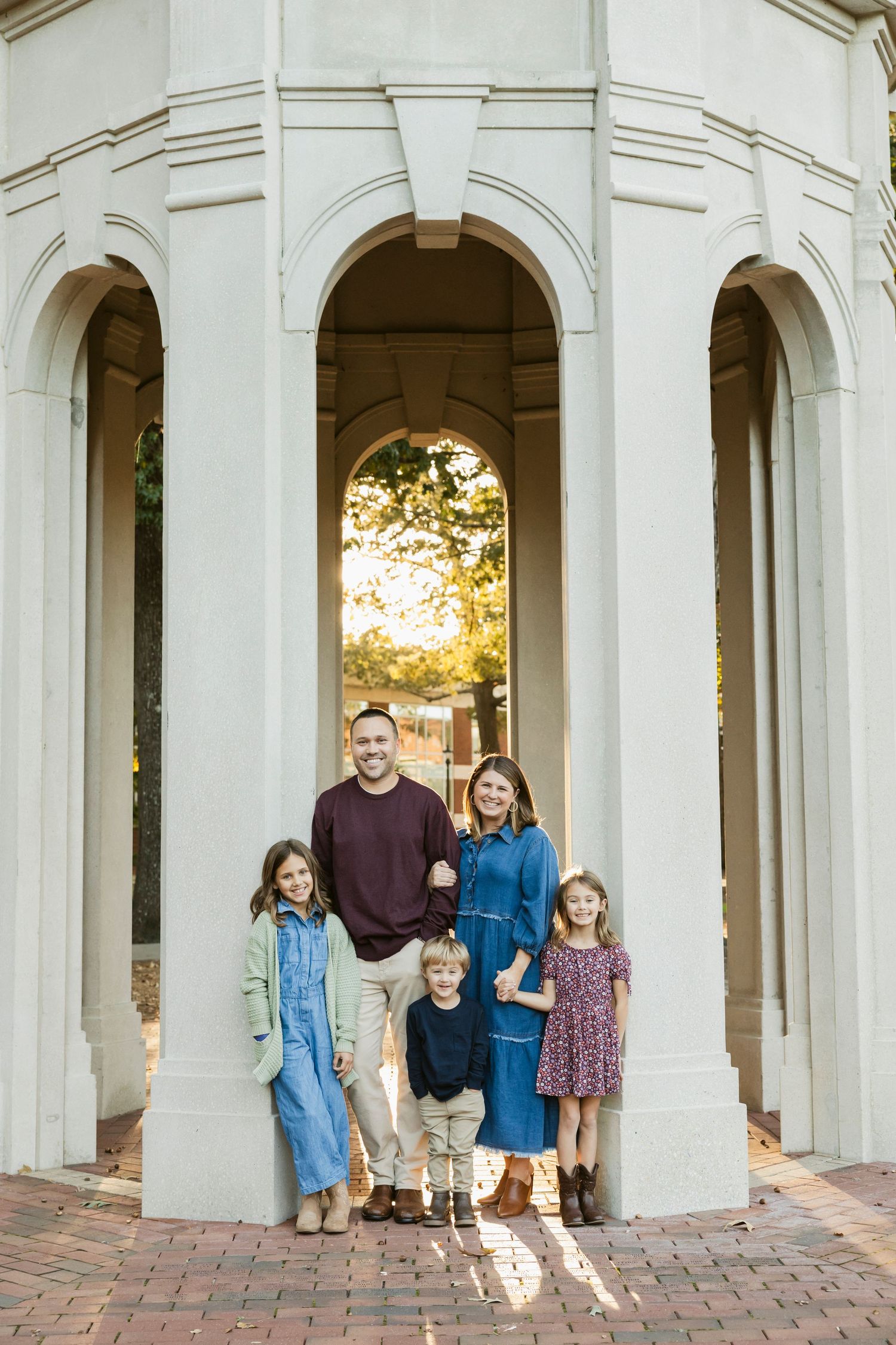 A family poses together under white arched columns during a portrait session.