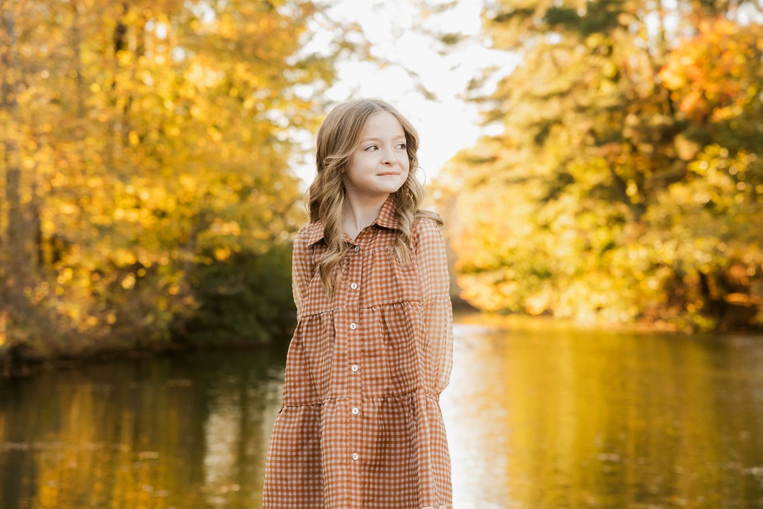 Golden autumn trees reflect in a serene lake during a fall photoshoot.
