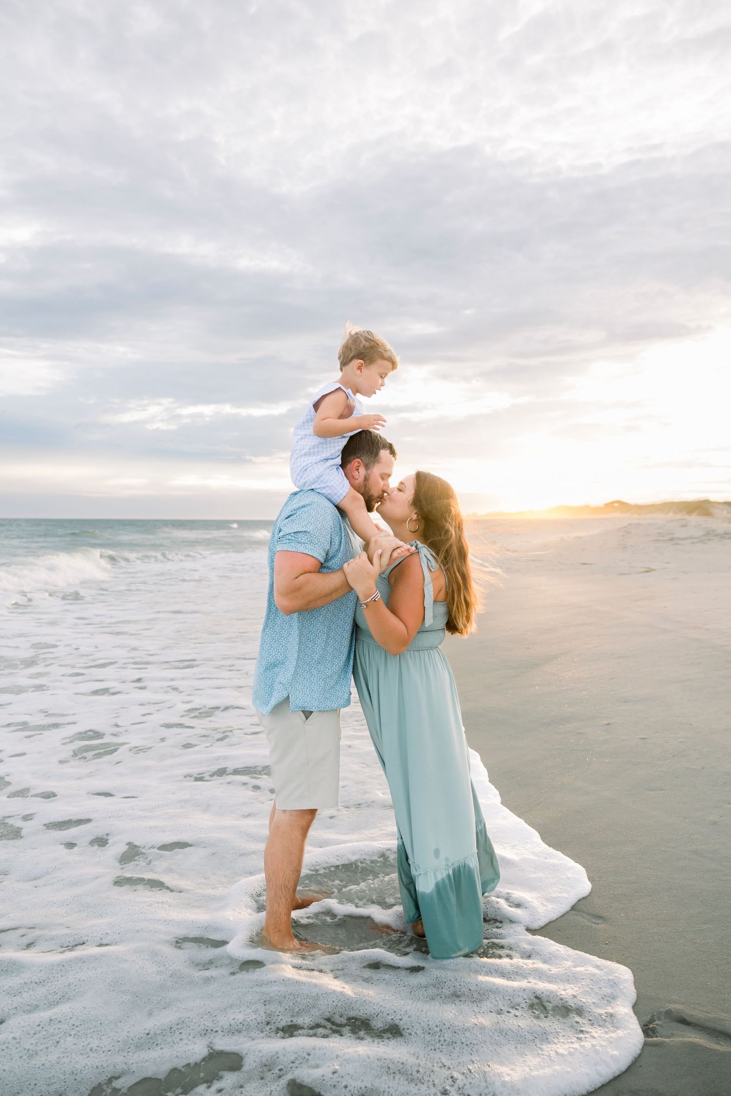 Couple embracing on beach during golden hour with waves crashing nearby.