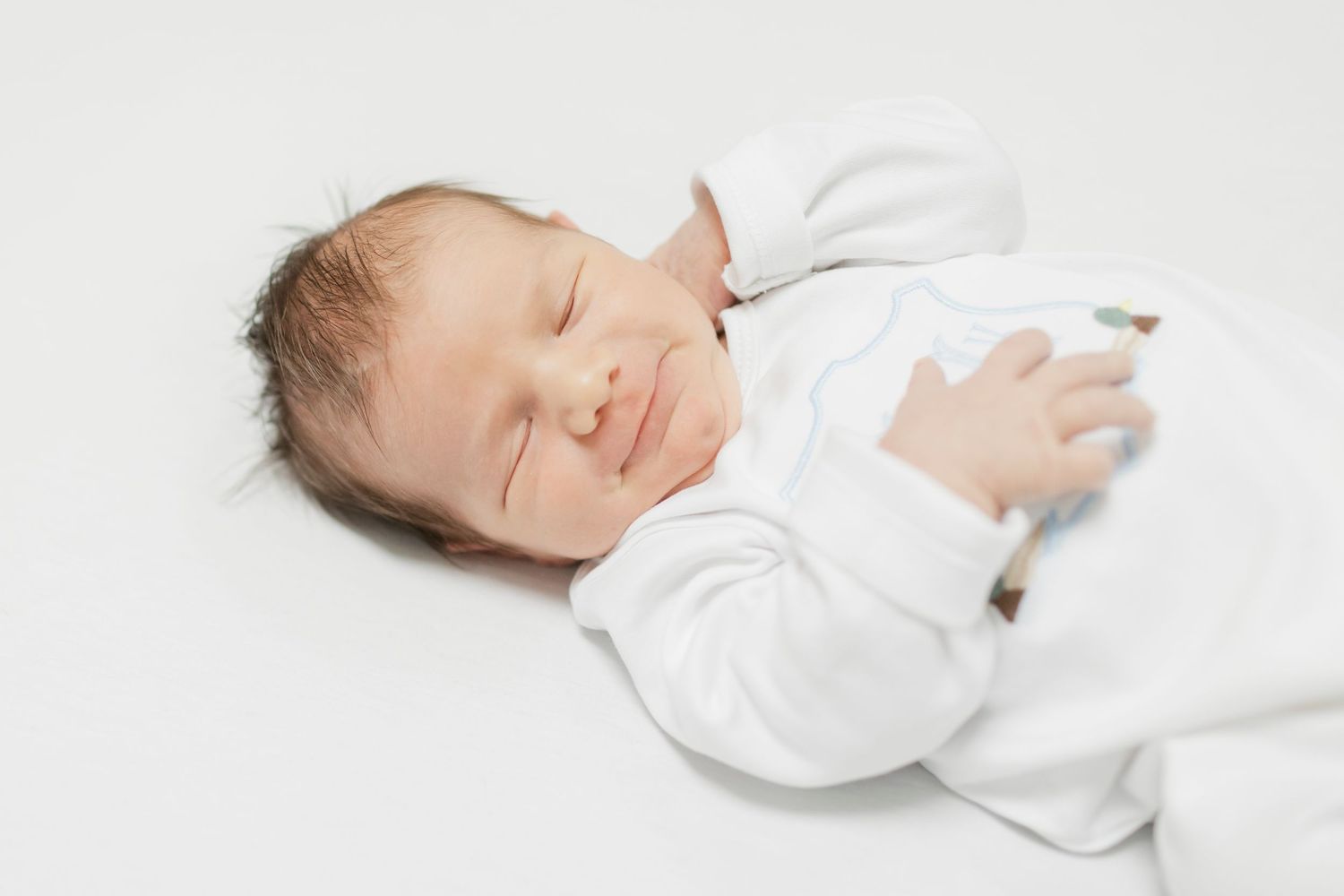 A peaceful sleeping newborn in white clothing against a white background.