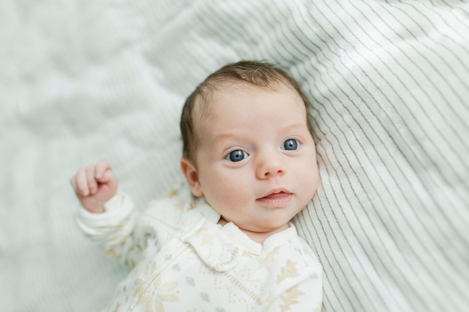 A small infant in white clothing lies on light colored bedding.