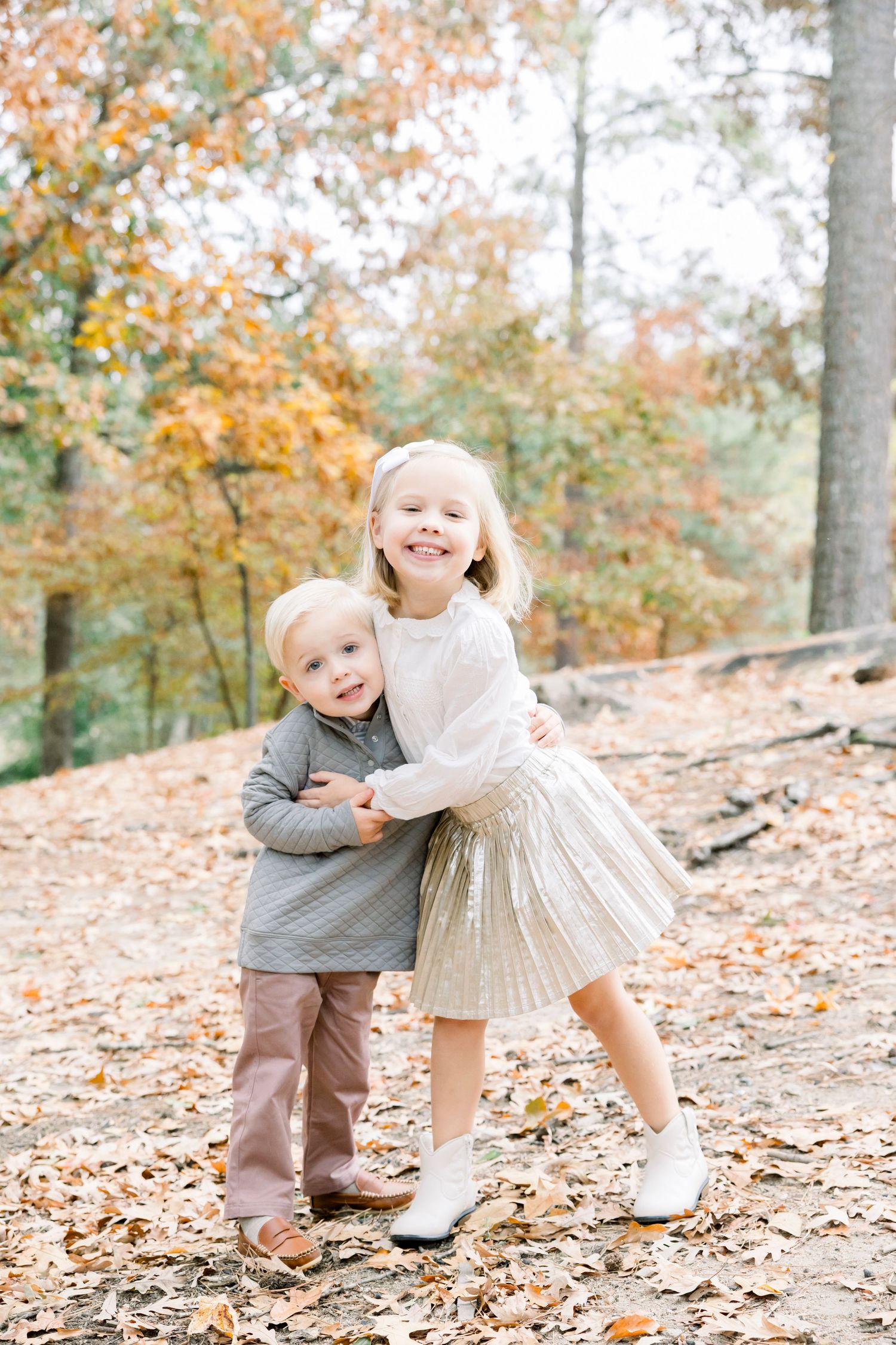 Two children playing together in autumn leaves on a forest floor.