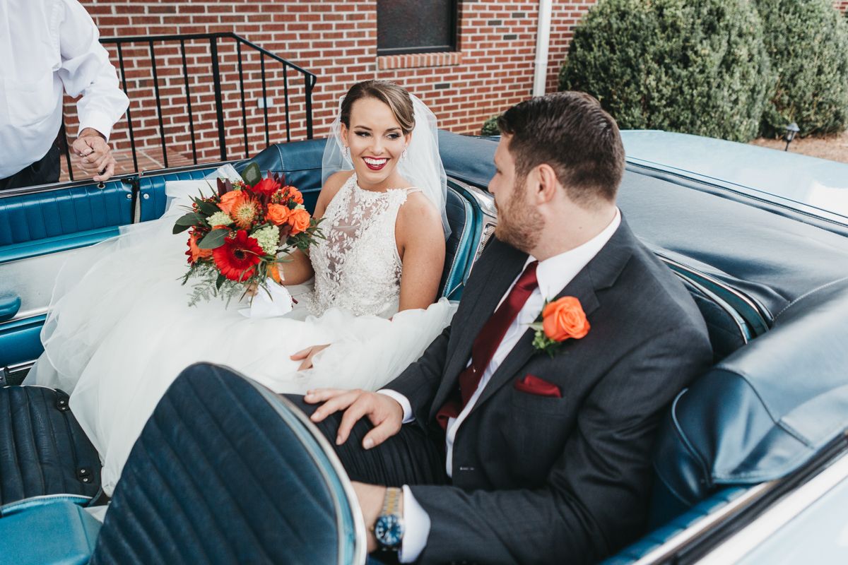 Newlyweds share a moment in a vintage blue car decorated for their wedding day.