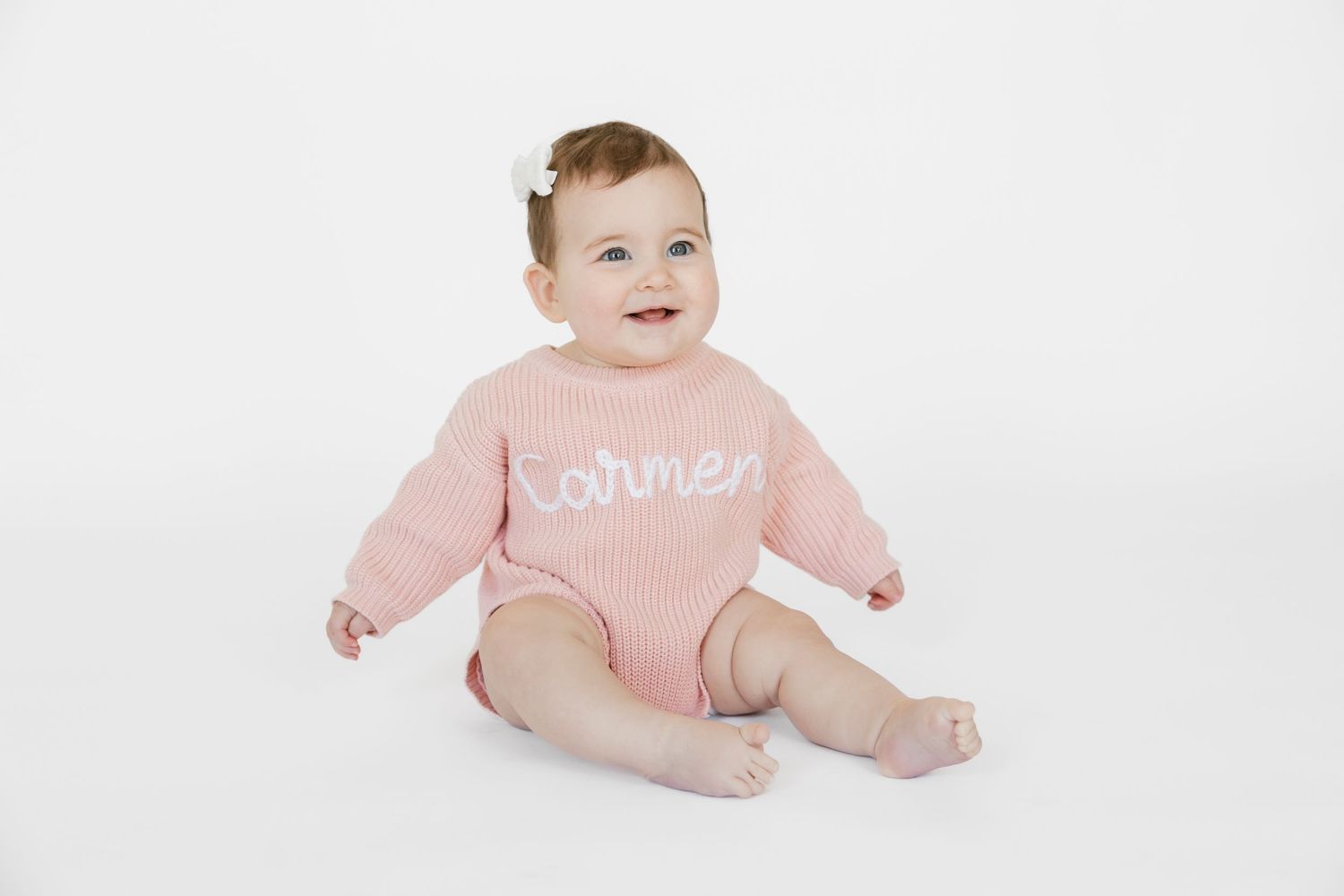 Baby wearing pink outfit crawling on white studio backdrop.