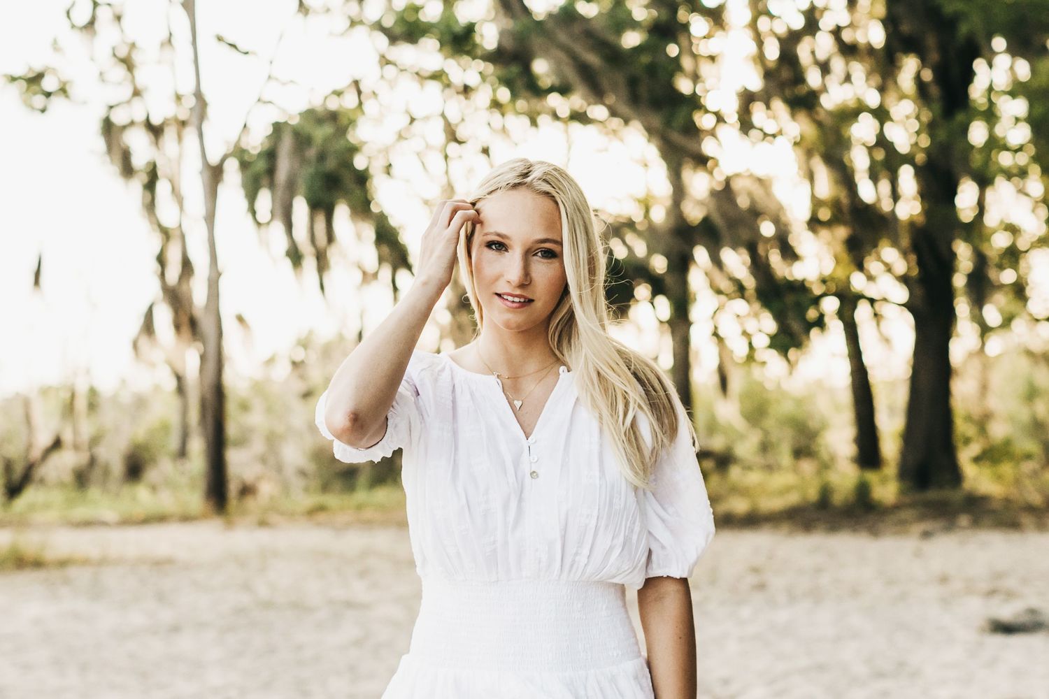 Woman in white dress walking through sunlit field during golden hour.