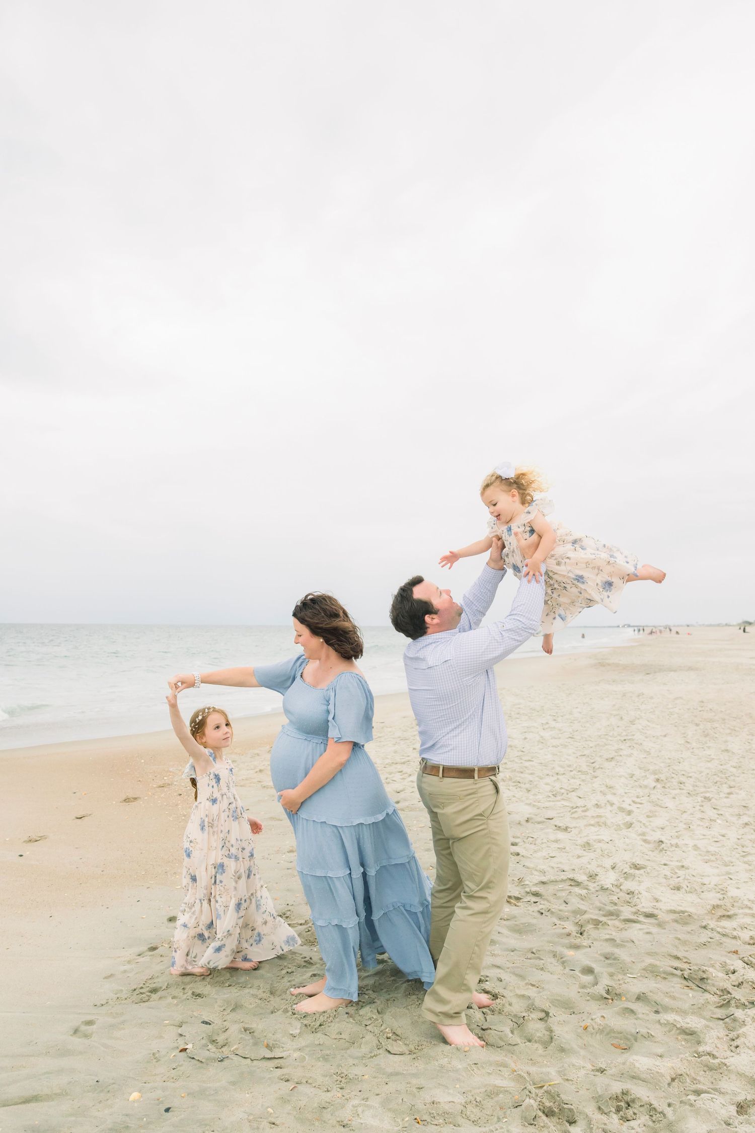 Playful beach photoshoot with family striking fun poses on sandy shore at sunset.