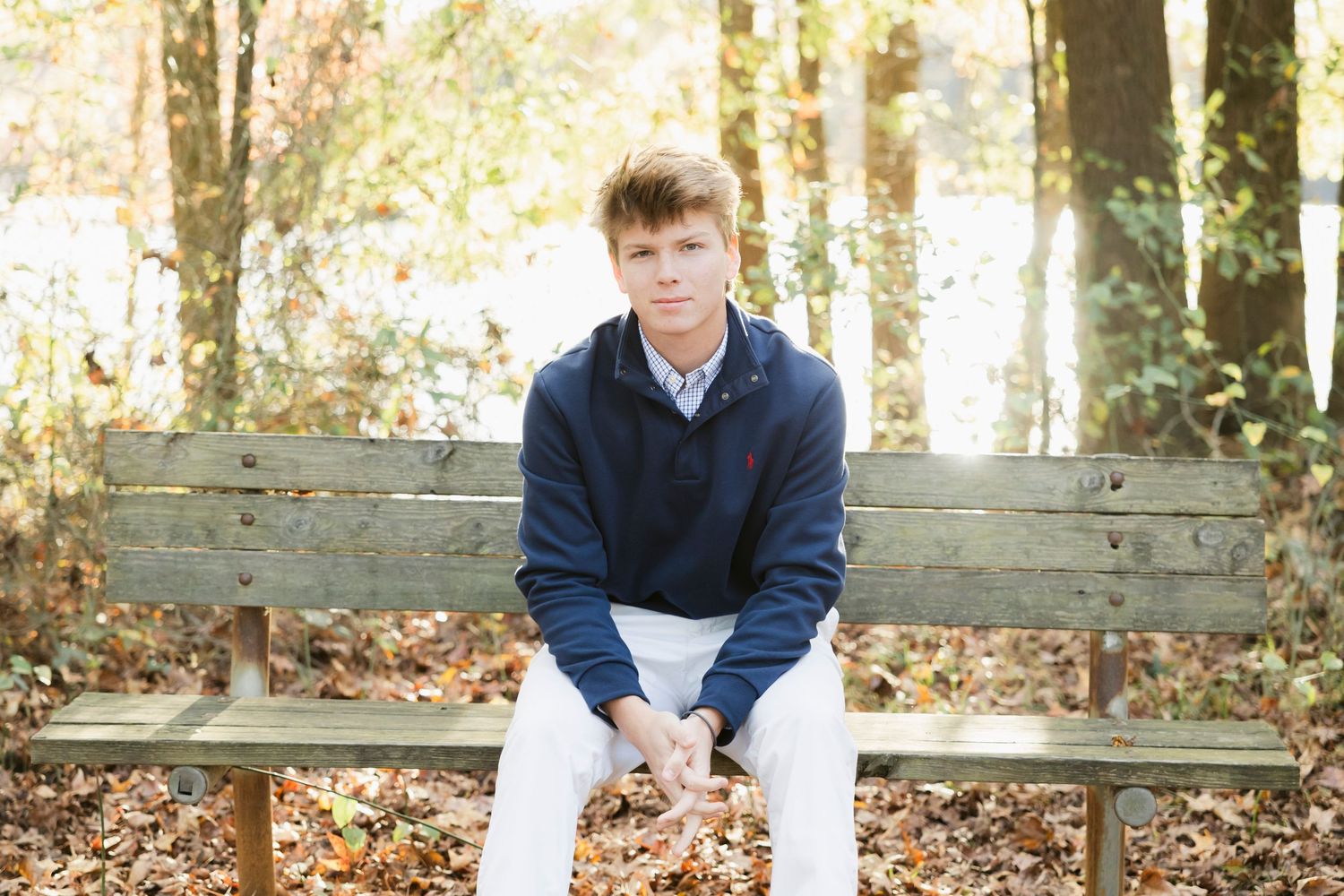 Person sitting on wooden bench surrounded by fallen autumn leaves.