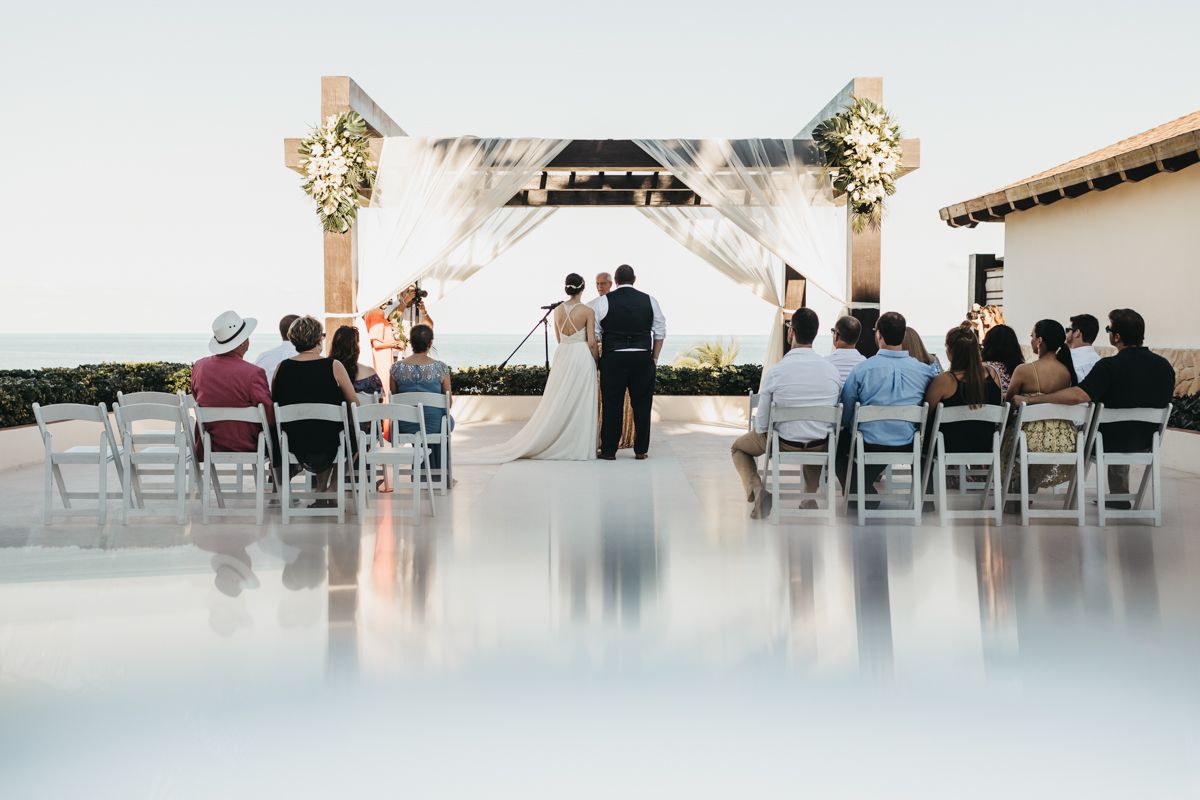 Wide angle view of an elegant white wedding ceremony setup with chairs and floral arrangements.