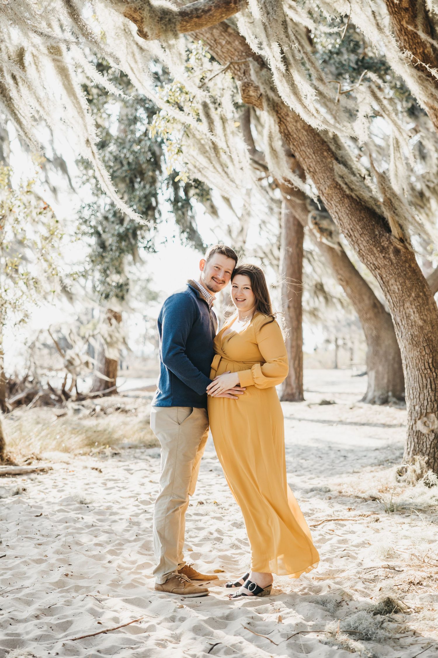 A couple shares intimate moments under Spanish moss-draped trees in warm sunlight.