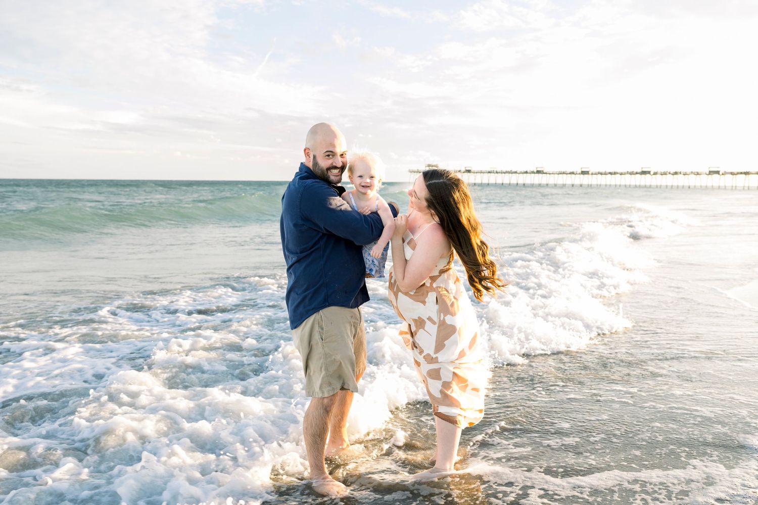 Couple playing in ocean waves during beach maternity photoshoot.
