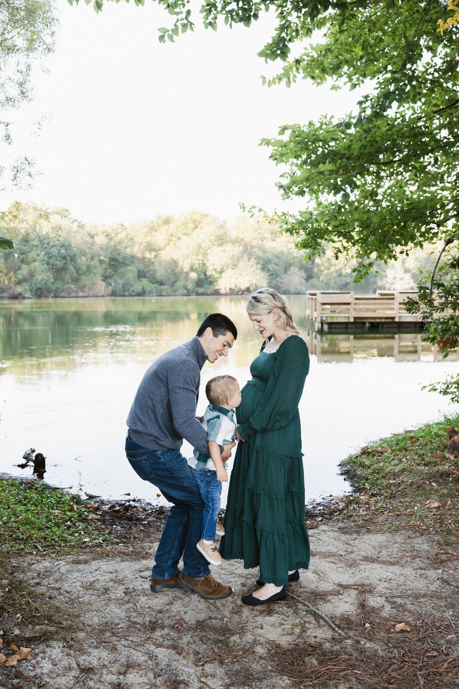 Pregnancy announcement photos by lakeside dock surrounded by autumn trees.