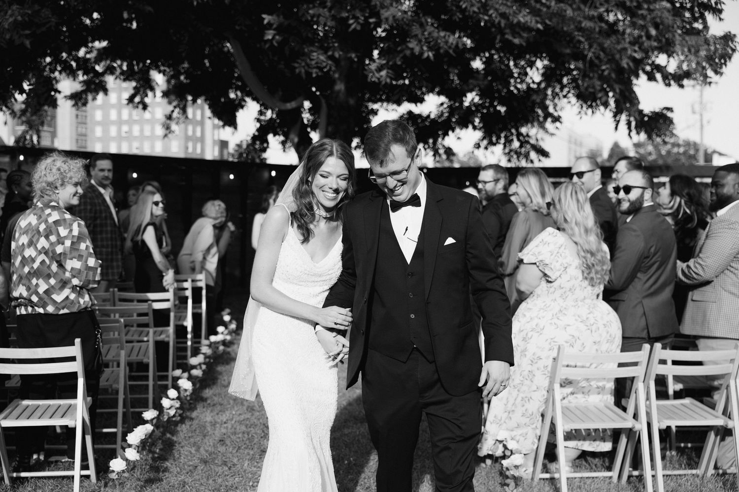 Wedding ceremony setup with white chairs arranged outdoors under large trees.