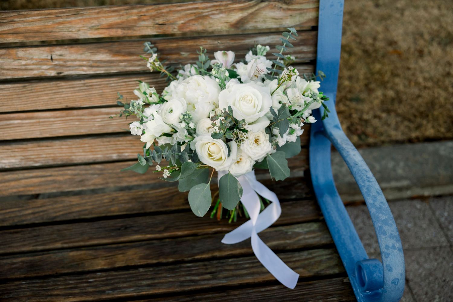 White and cream floral wedding bouquet with roses and greenery resting on weathered blue wooden surface.
