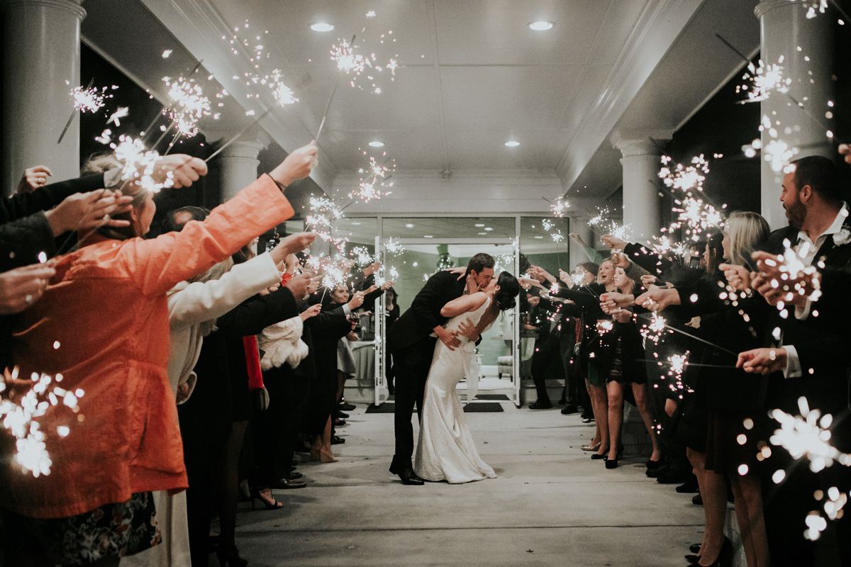 Wedding guests create a sparkler exit tunnel for the newlyweds in an indoor venue.