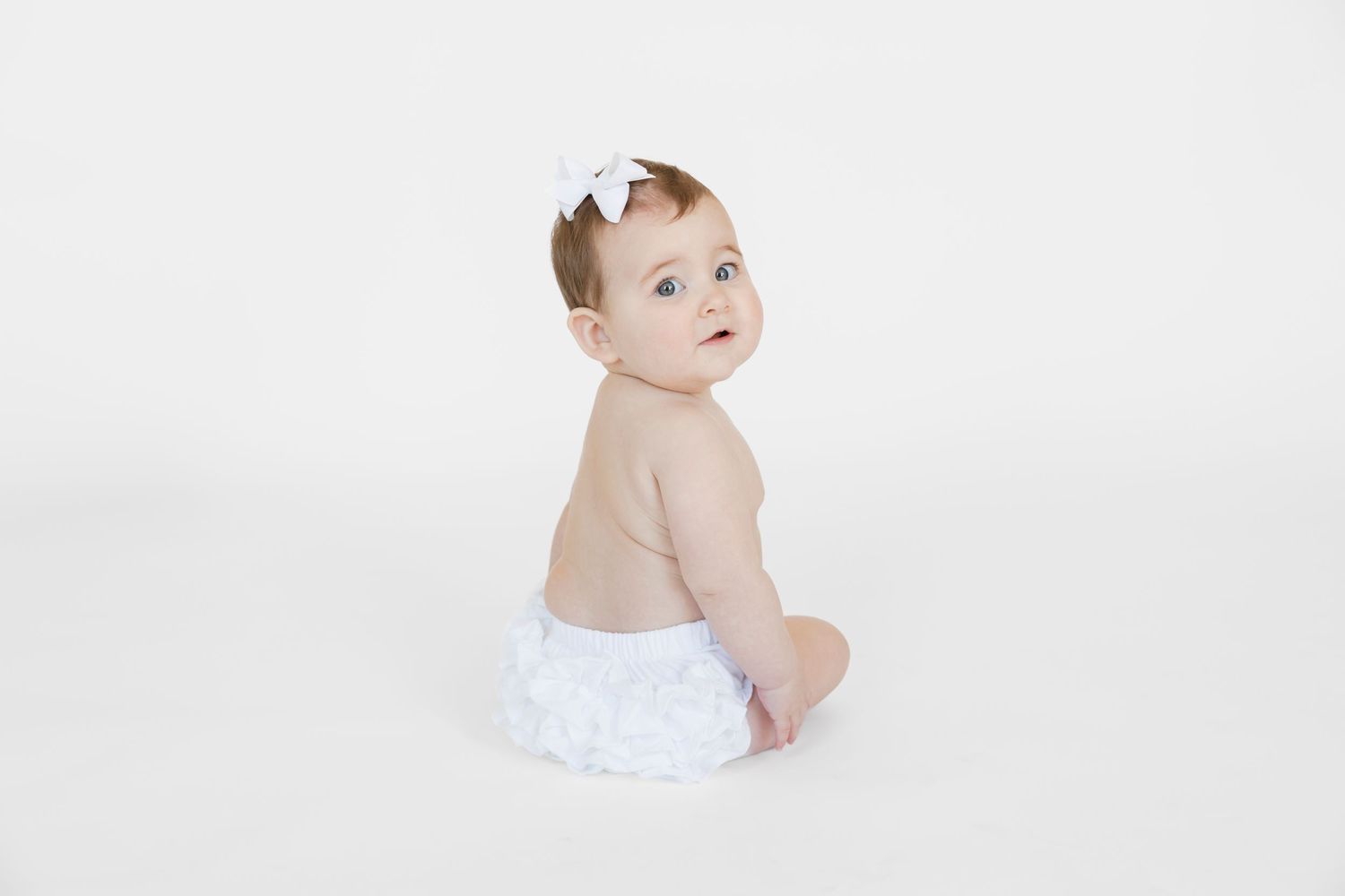 Baby wearing white bow crawling on white studio floor.