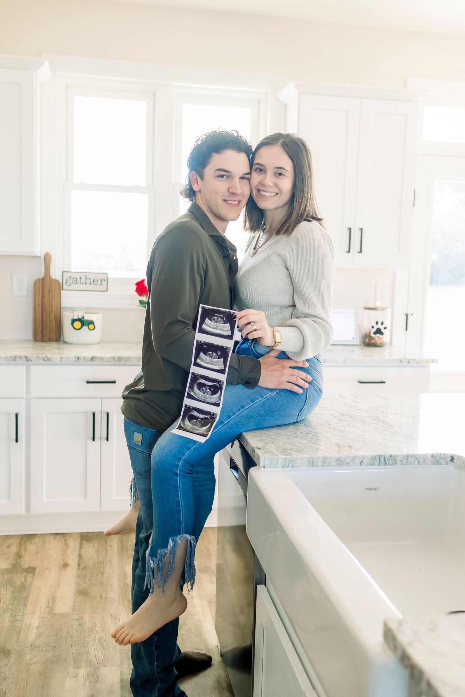 Couple sharing ultrasound photos while sitting on kitchen counter in bright modern home.