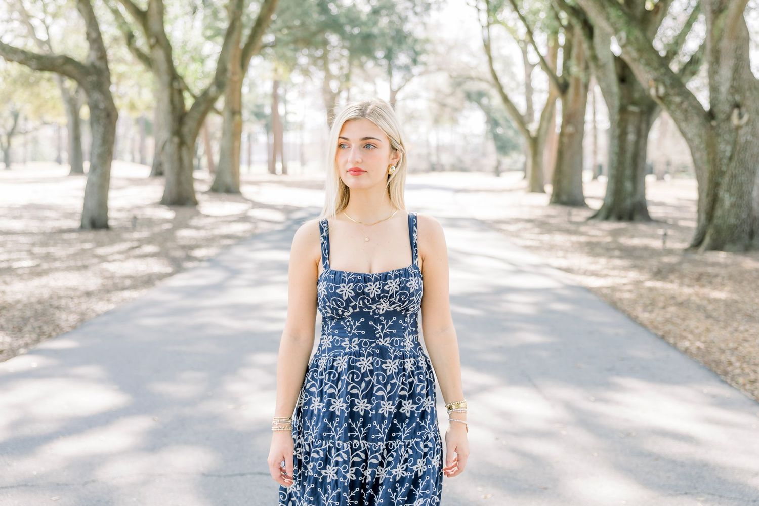 Person in blue floral dress walking along tree-lined path.