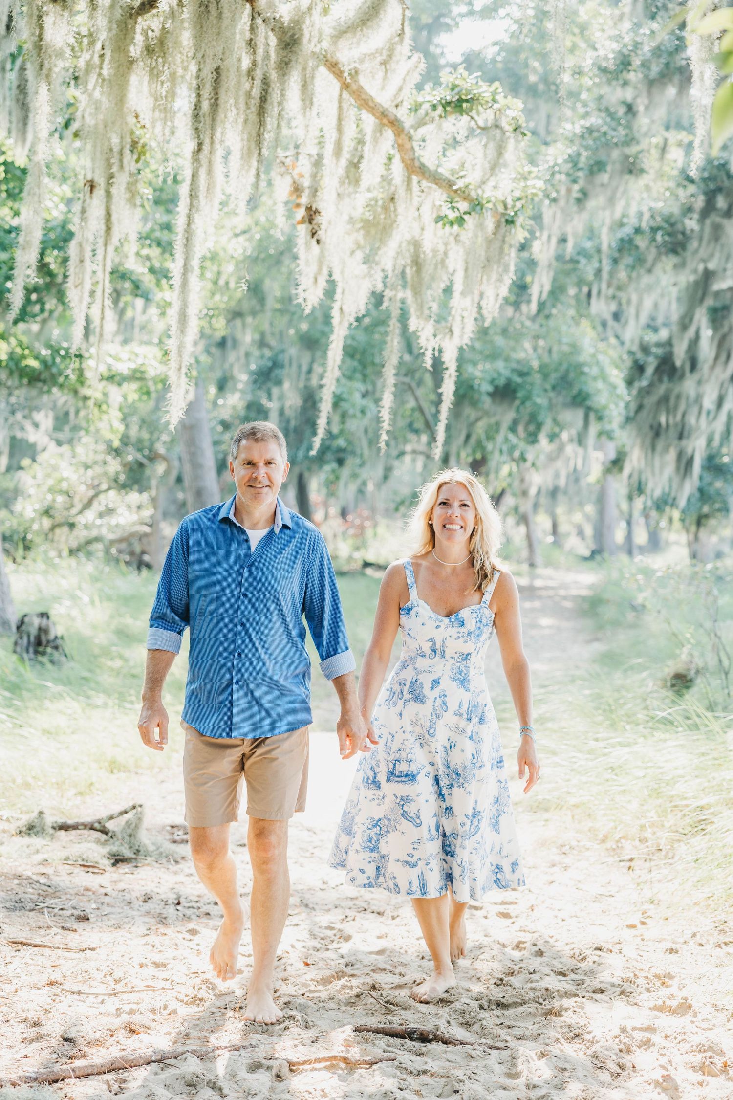 Couple walking hand in hand on a path under Spanish moss draped trees.