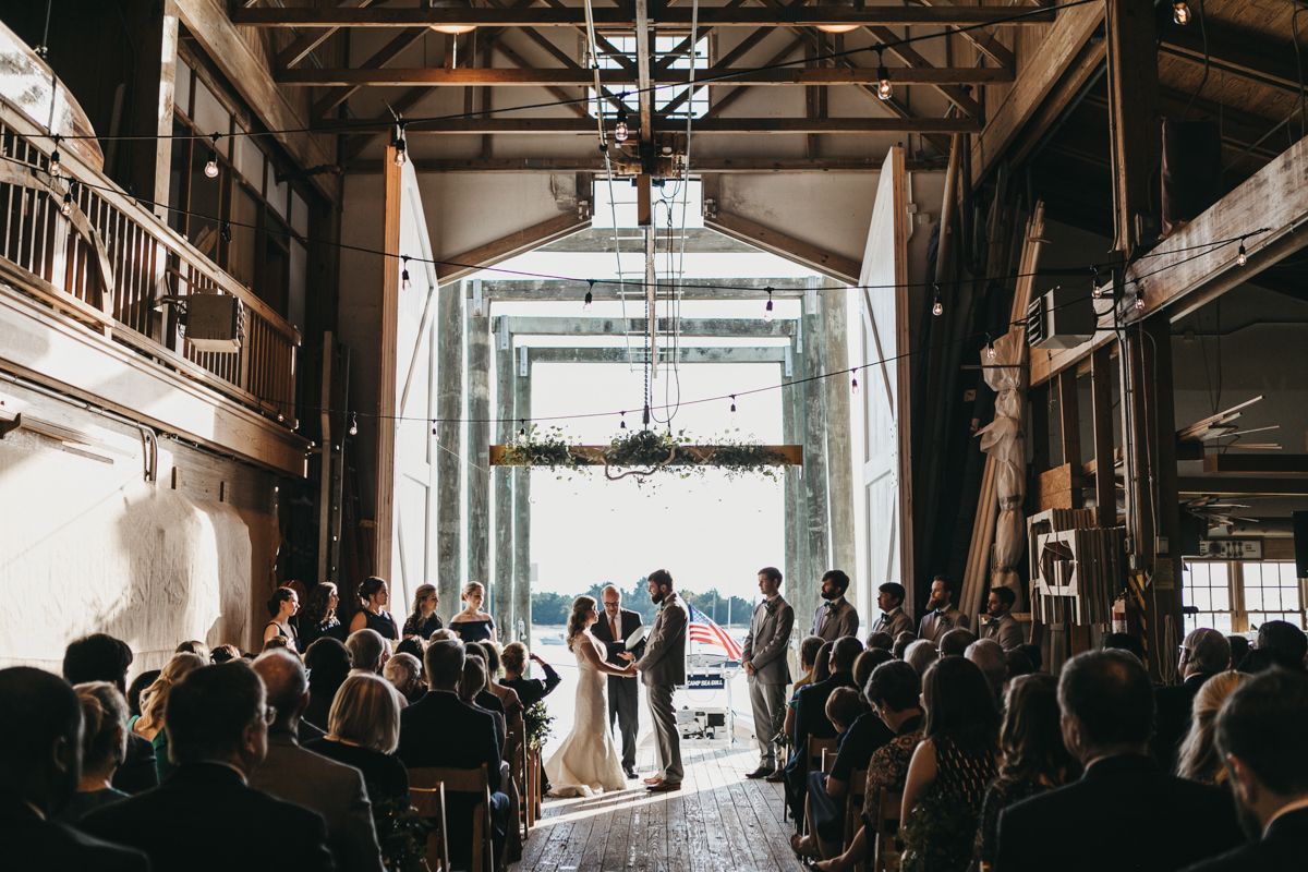 Wedding ceremony setup in an industrial venue with exposed beams and natural lighting.
