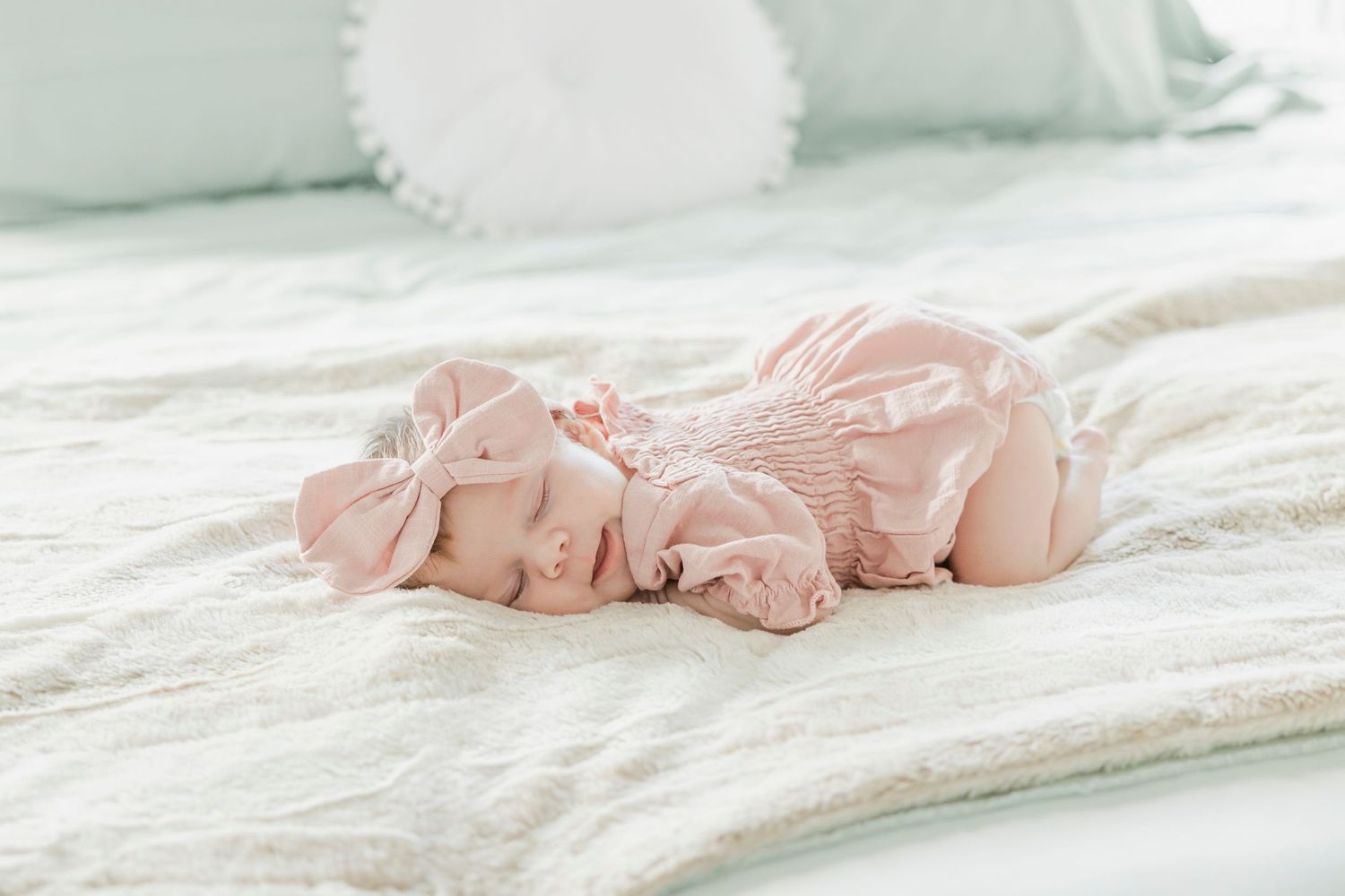 Sleeping baby in pink outfit lying on white textured bedding.