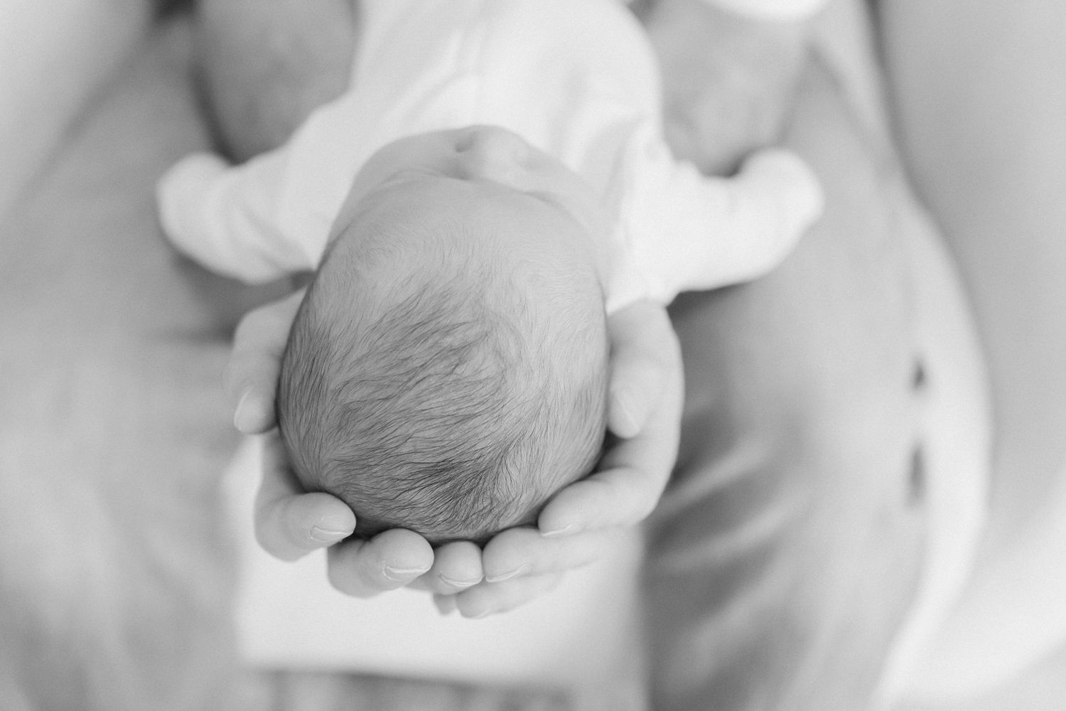 Black and white image of tiny newborn baby's head cradled in gentle hands.