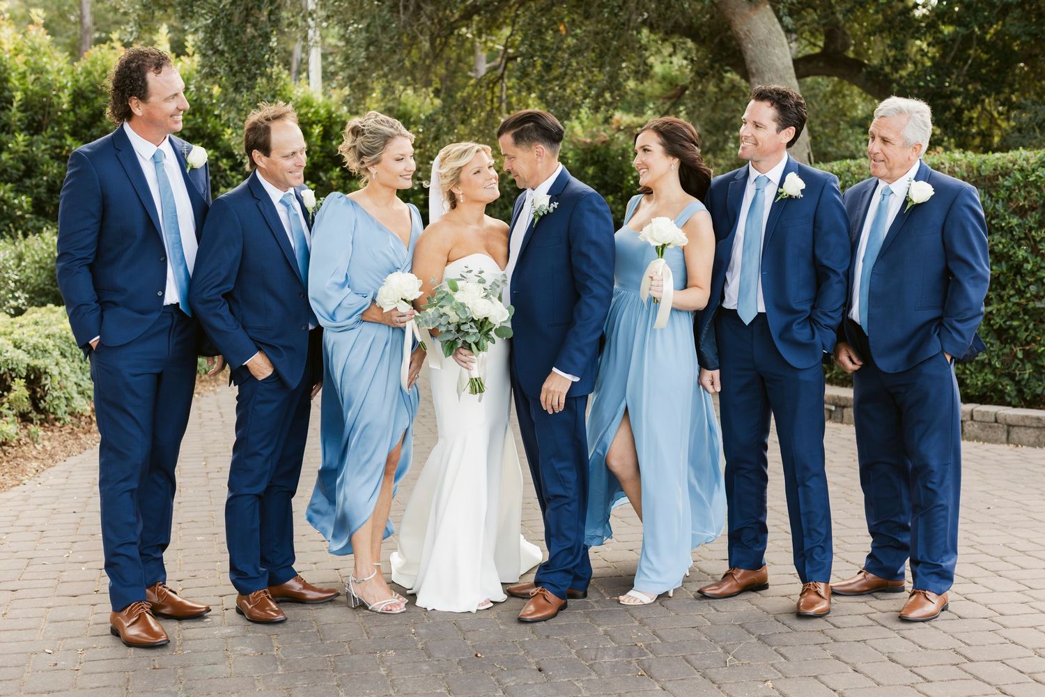 Wedding party in navy suits and light blue dresses poses together outdoors.