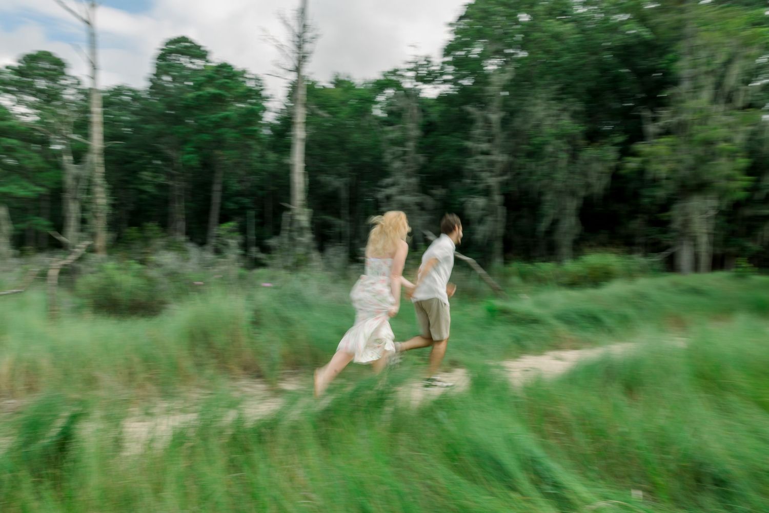People playfully run through tall grass in a dynamic outdoor photoshoot sequence.