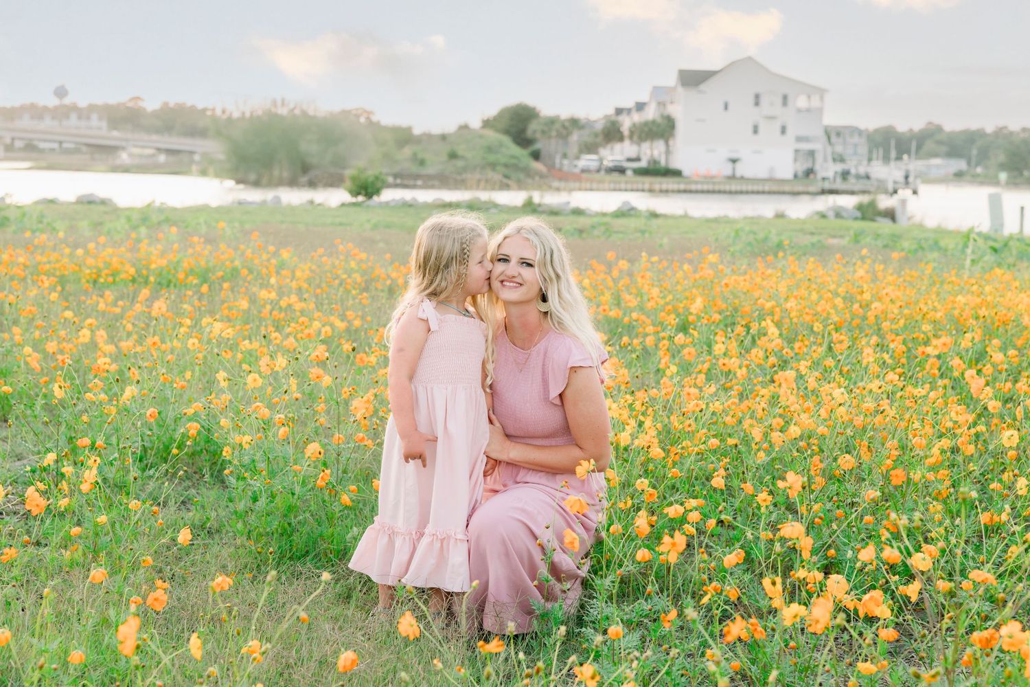Two figures in pink dresses pose together in a vibrant field of yellow wildflowers on a sunny day.