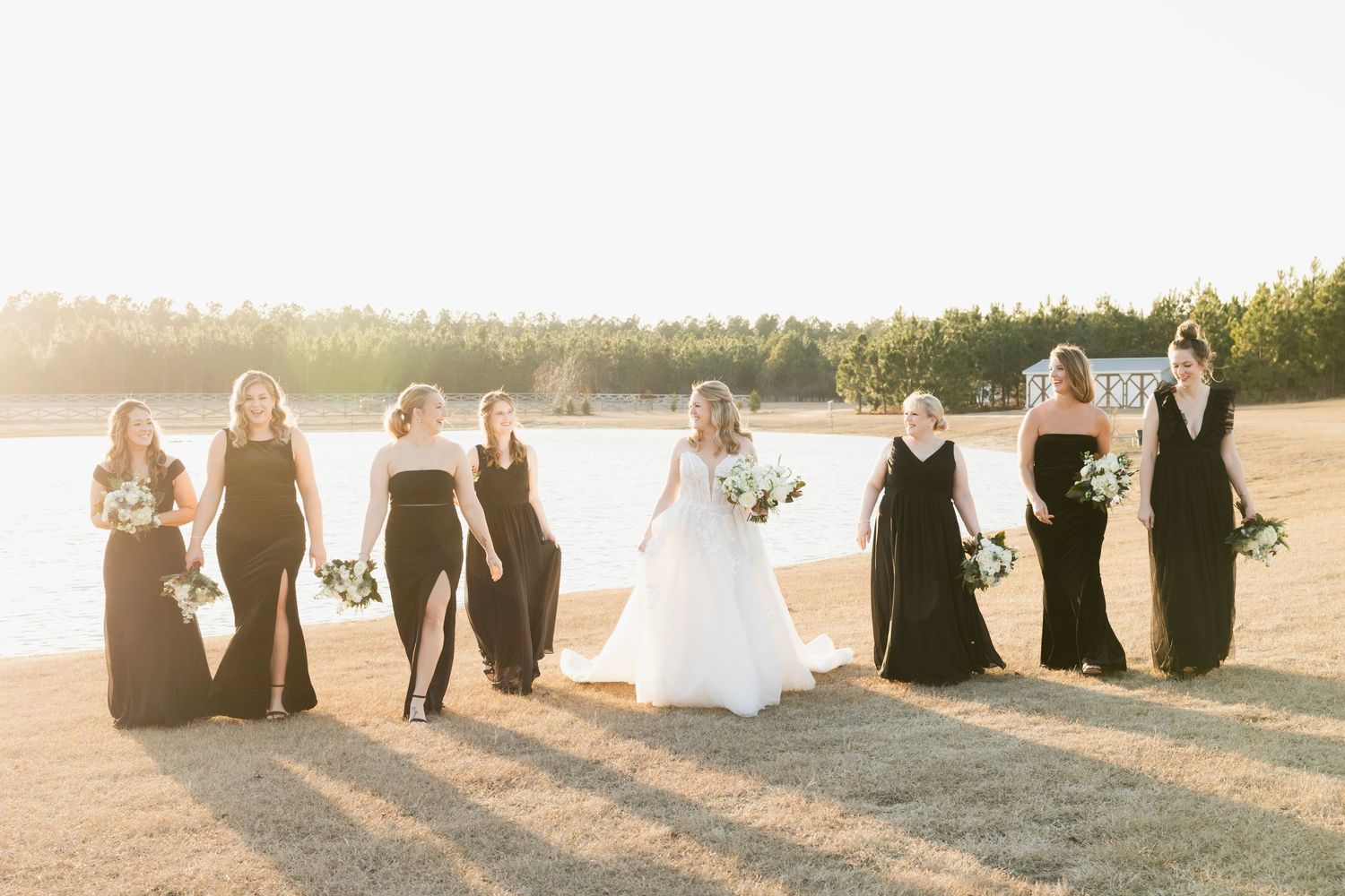 Wedding party in formal attire stands together on a stone patio at sunset.