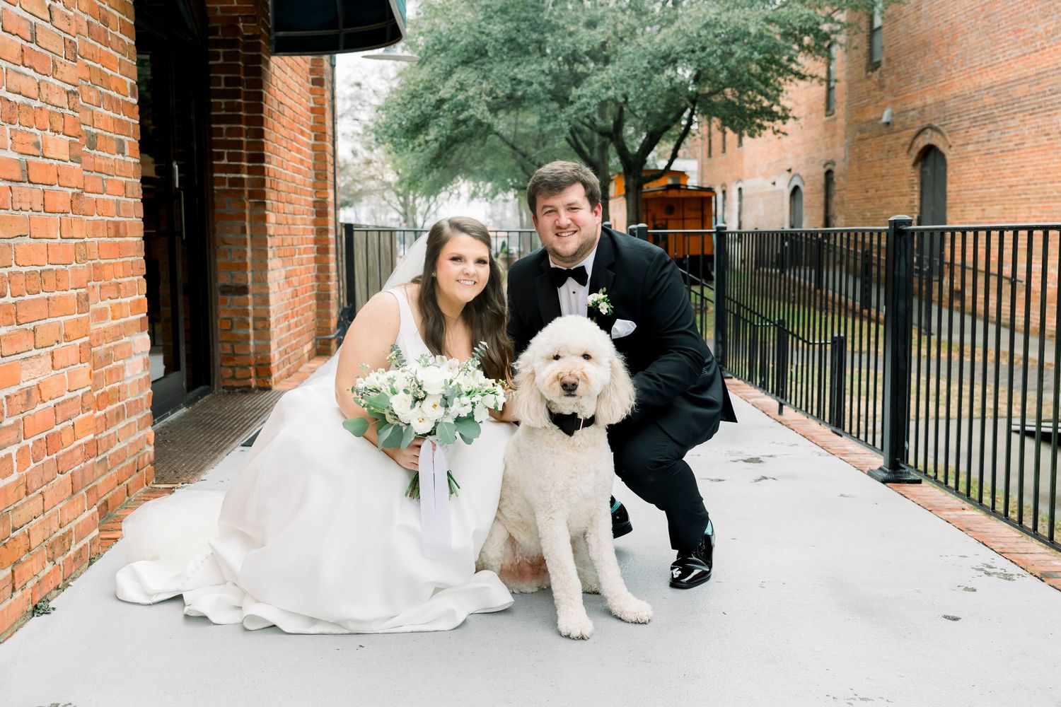 Wedding couple poses with their dog outside brick church building.
