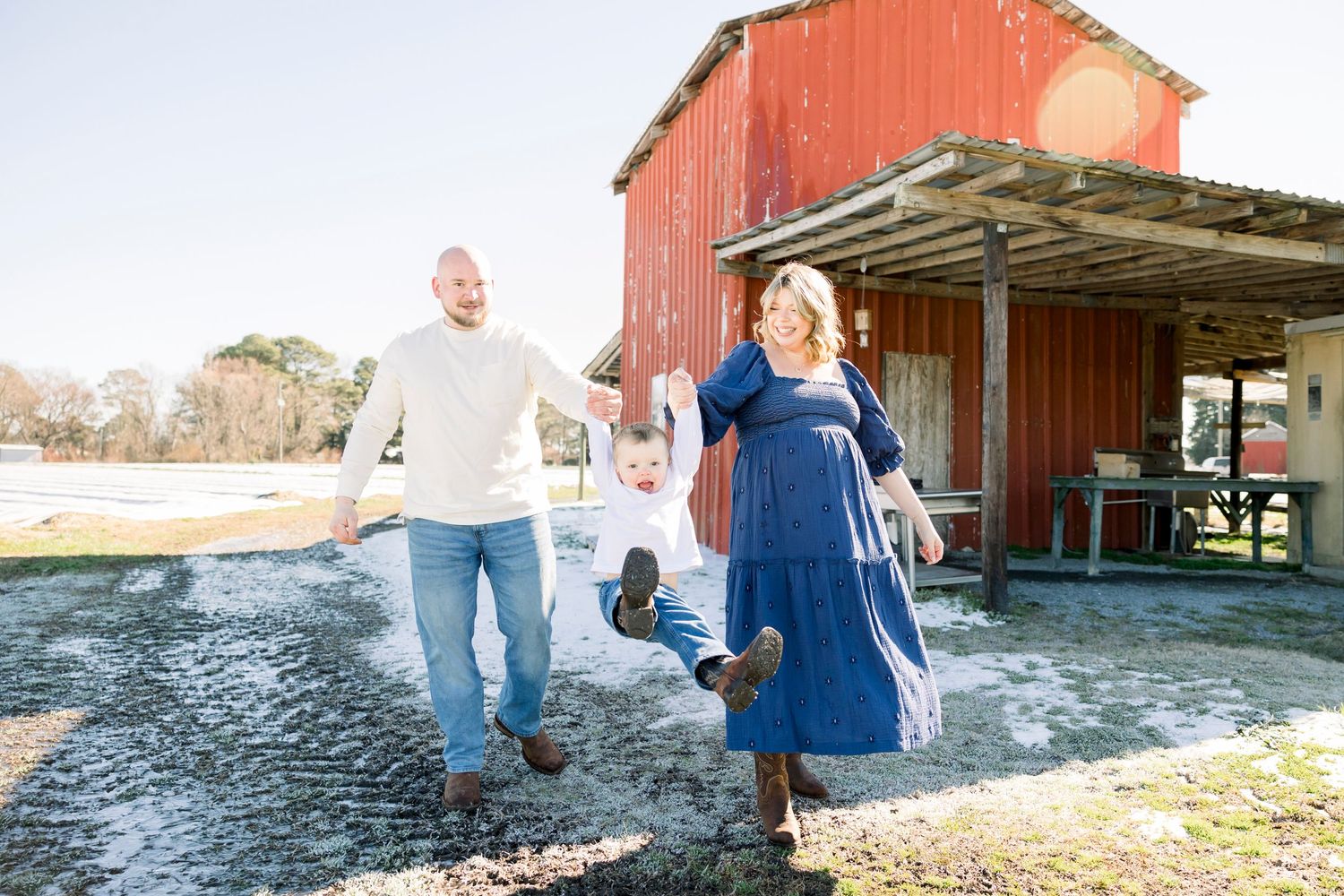 Candid moments captured near a rustic red barn during golden hour.