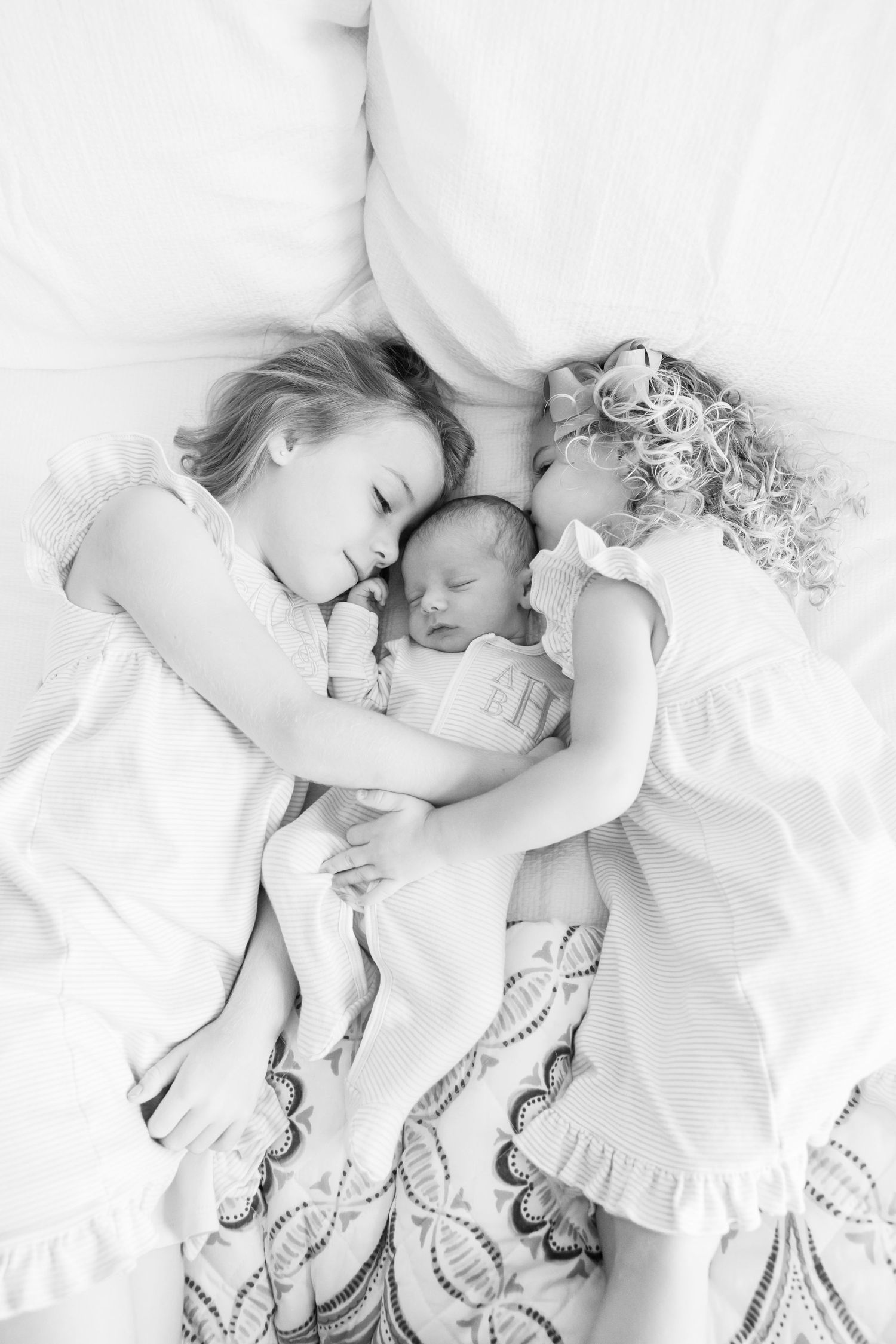 Black and white image of siblings sleeping together on floral patterned bedding.