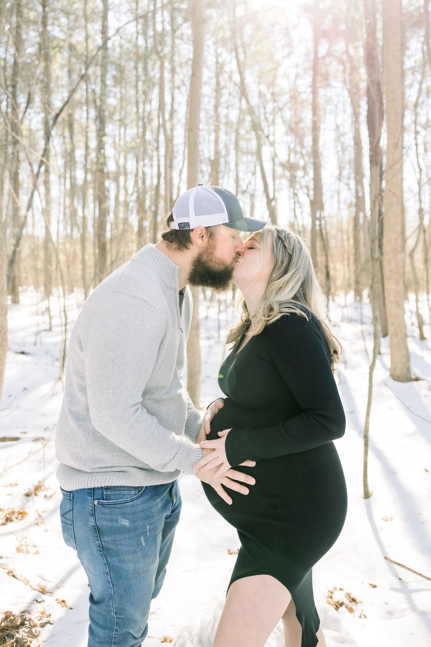 A couple poses together in a snowy winter forest setting.