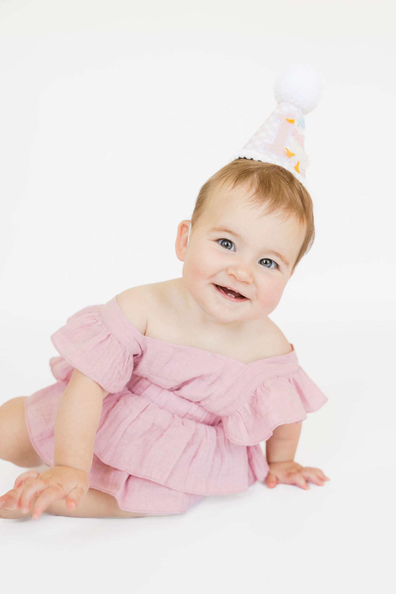 Infant wearing pink ruffle dress lying on white floor.