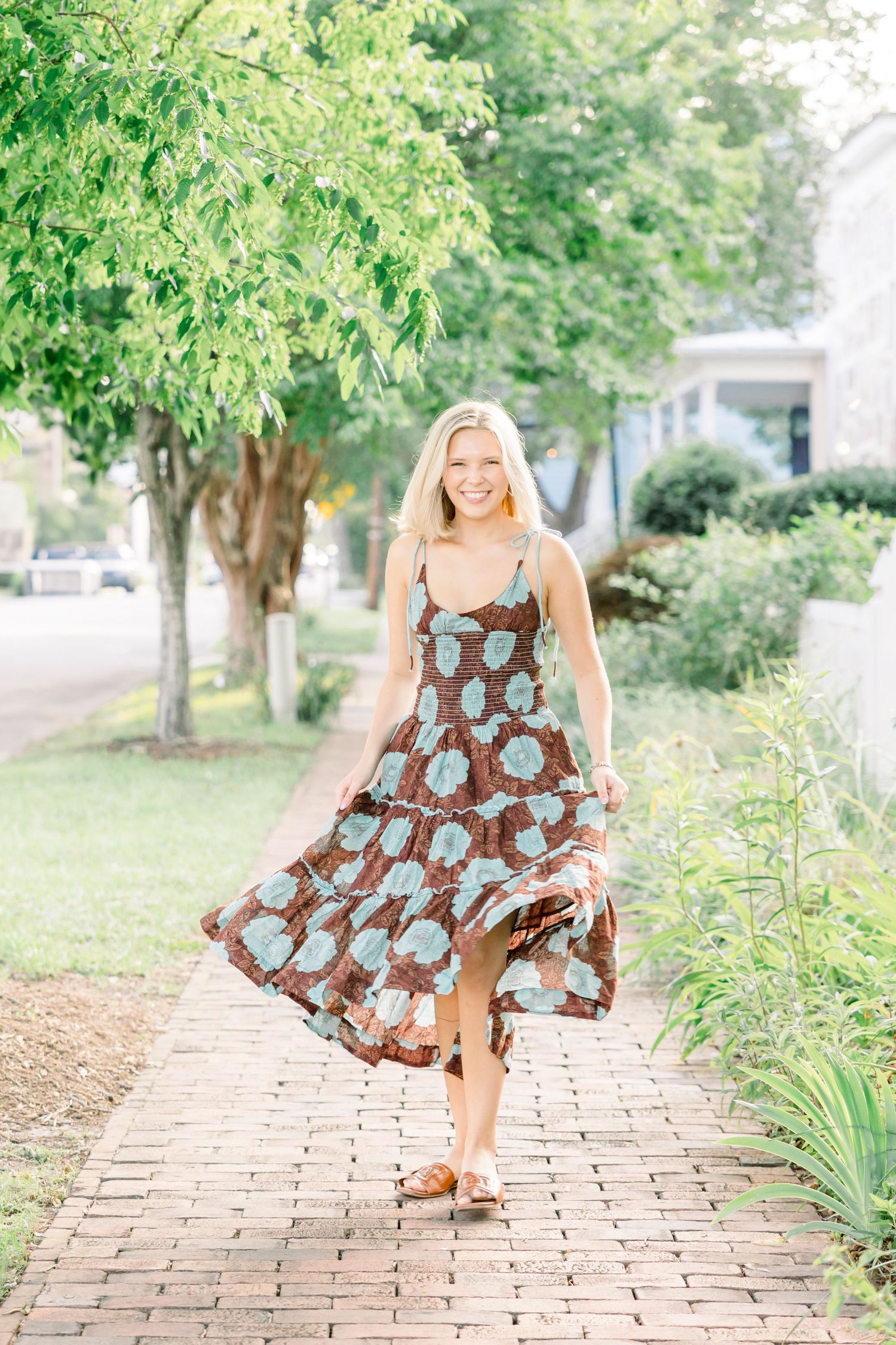 Someone twirling in a patterned dress on a brick pathway surrounded by lush greenery.