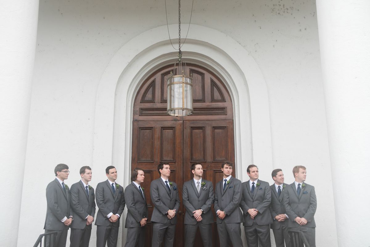 Wedding party in gray suits lined up in front of a classic white church building.