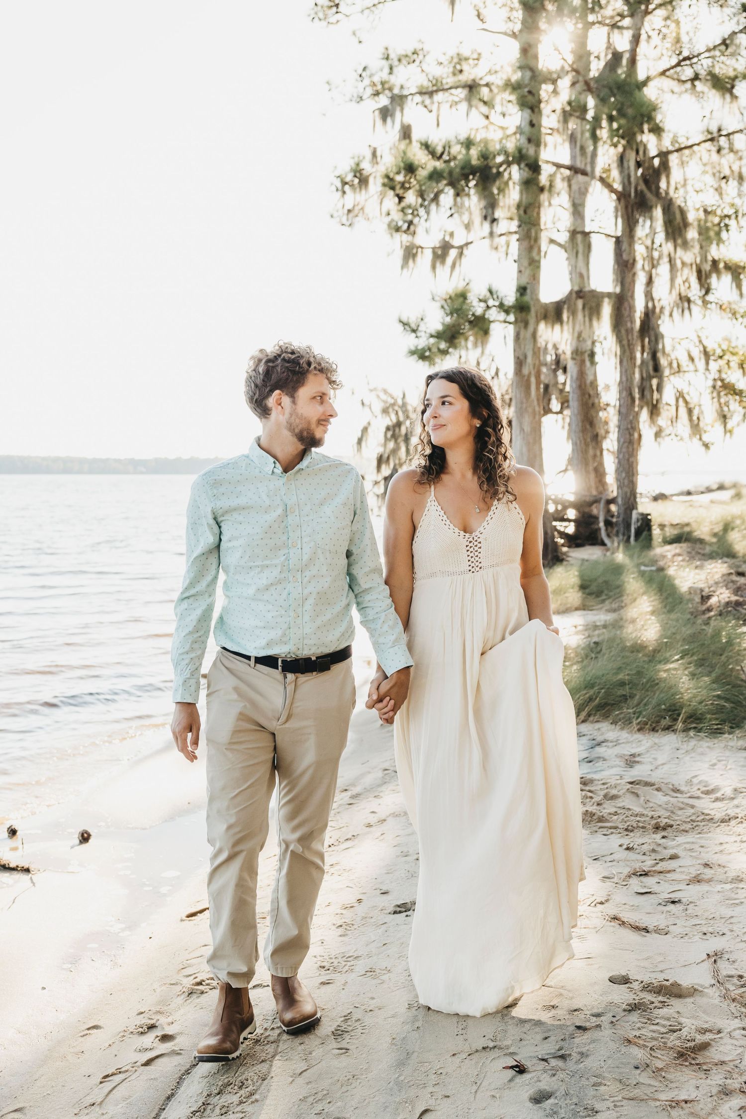 Couple strolls along tree-lined beach path in casual coastal wedding attire.