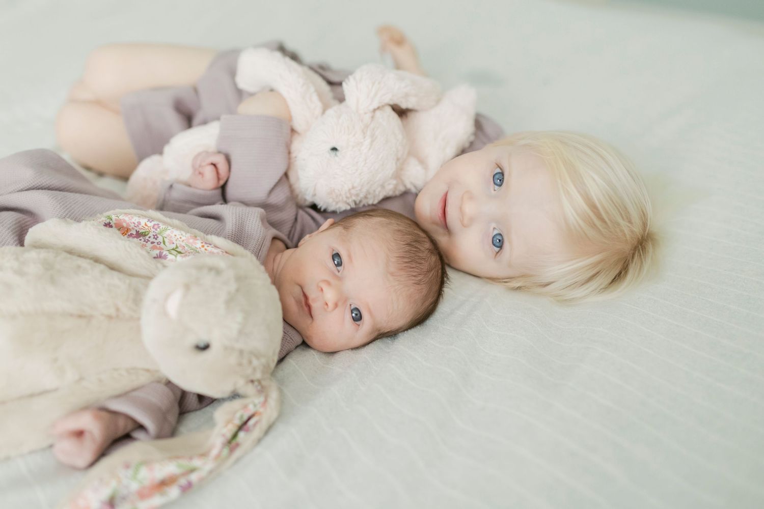 Baby in white outfit lying on mint green bedding.
