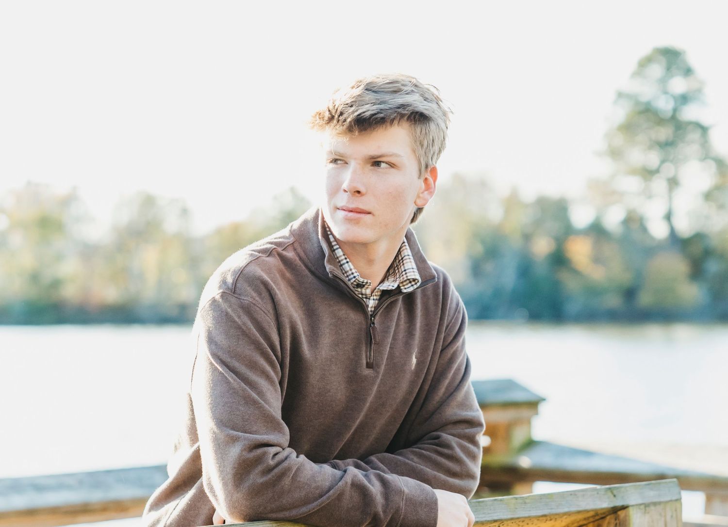 Person in brown sweater sitting on wooden bench near water.